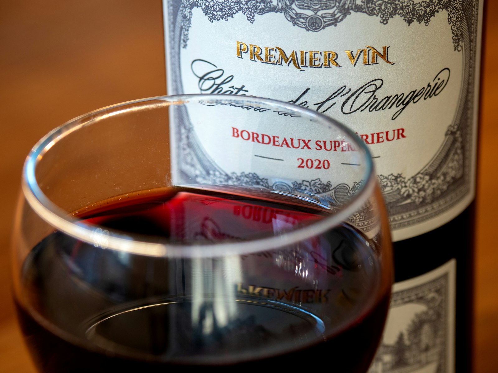 A glass of red Bordeaux held in front of a château wine label. Photo by Brett Jordan on Unsplash.