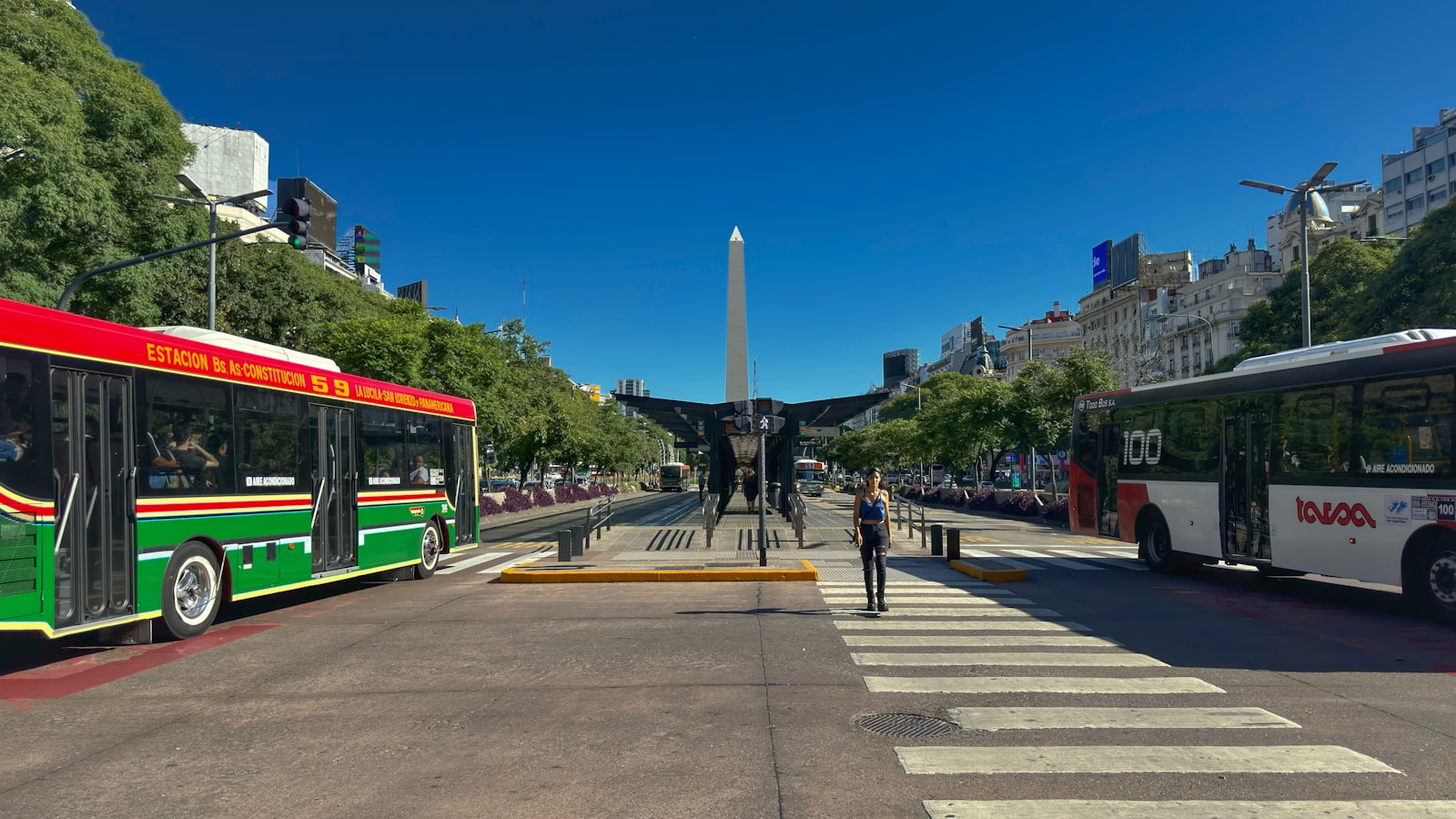 Colectivos y peatones en un cruce de una avenida ancha bajo el Obelisco de Buenos Aires. Foto de Juan Pablo Mascanfroni en Unsplash.