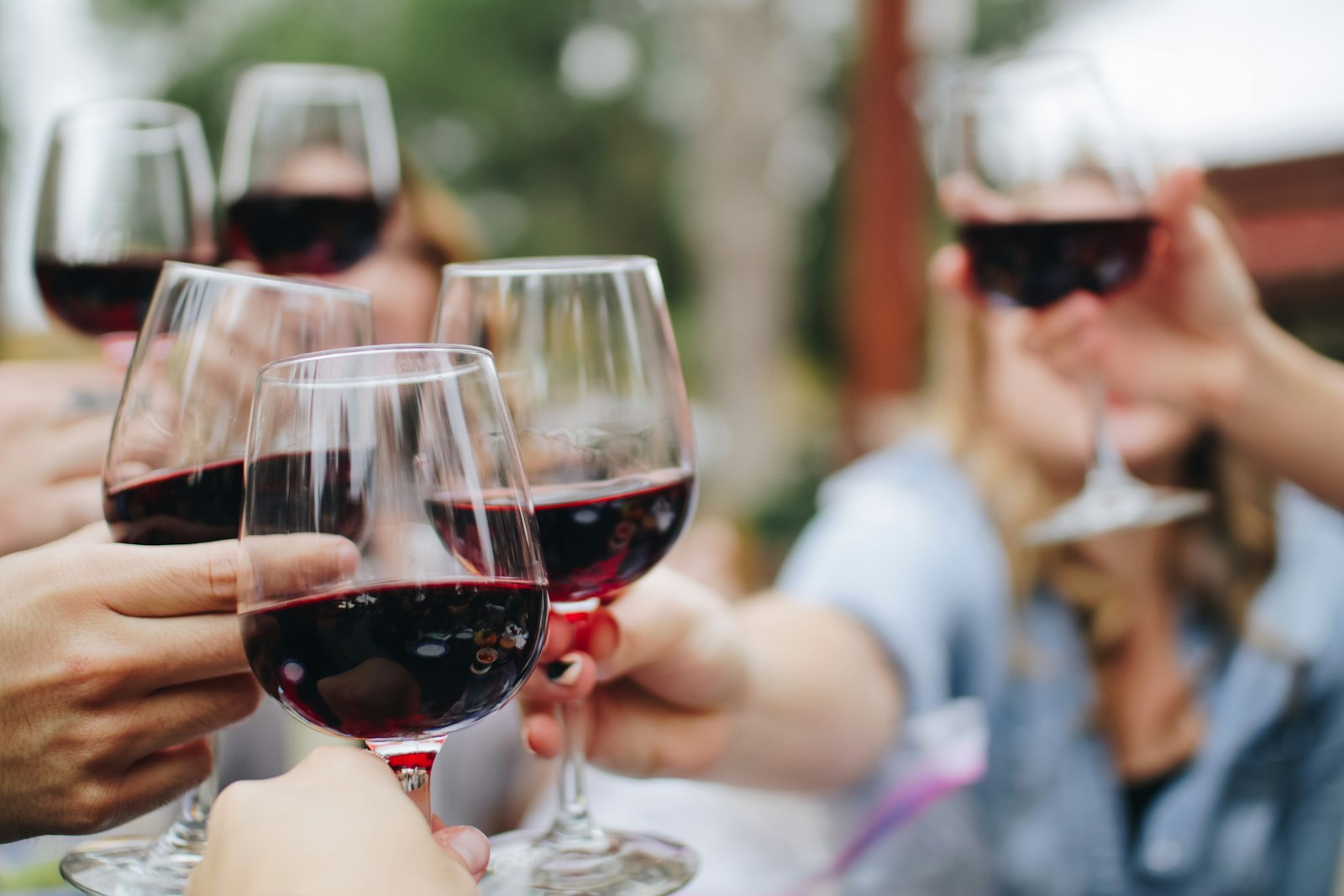 Friends clinking glasses of red wine together outdoors in wine country. Photo by Kelsey Knight on Unsplash.