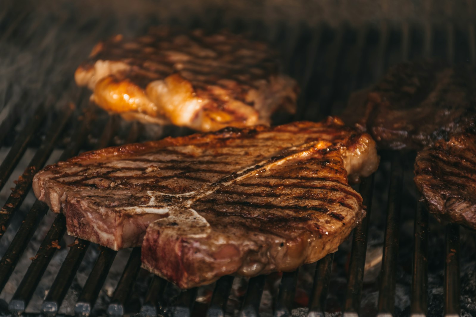 A thick T-bone steak searing over a charcoal grill, the way bistecca alla fiorentina is cooked. Photo by Hitesh Dewasi on Unsplash.