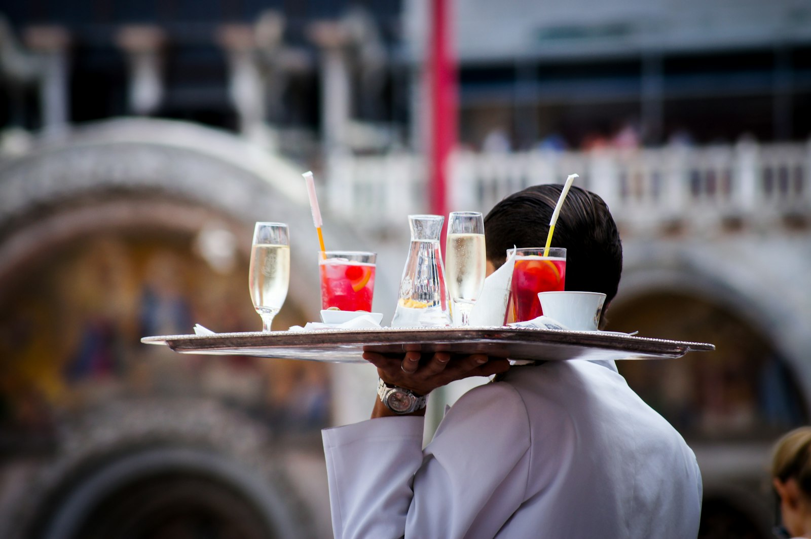 A waiter carries a tray of spritzes and prosecco flutes for an aperitivo. Photo by Kate Townsend on Unsplash.