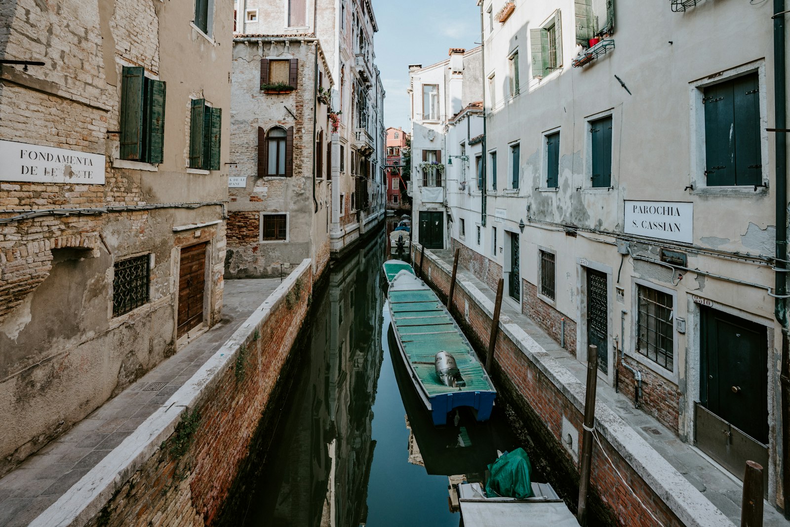 A boat moored on a quiet residential side canal between weathered Venetian houses. Photo by Annie Spratt on Unsplash.
