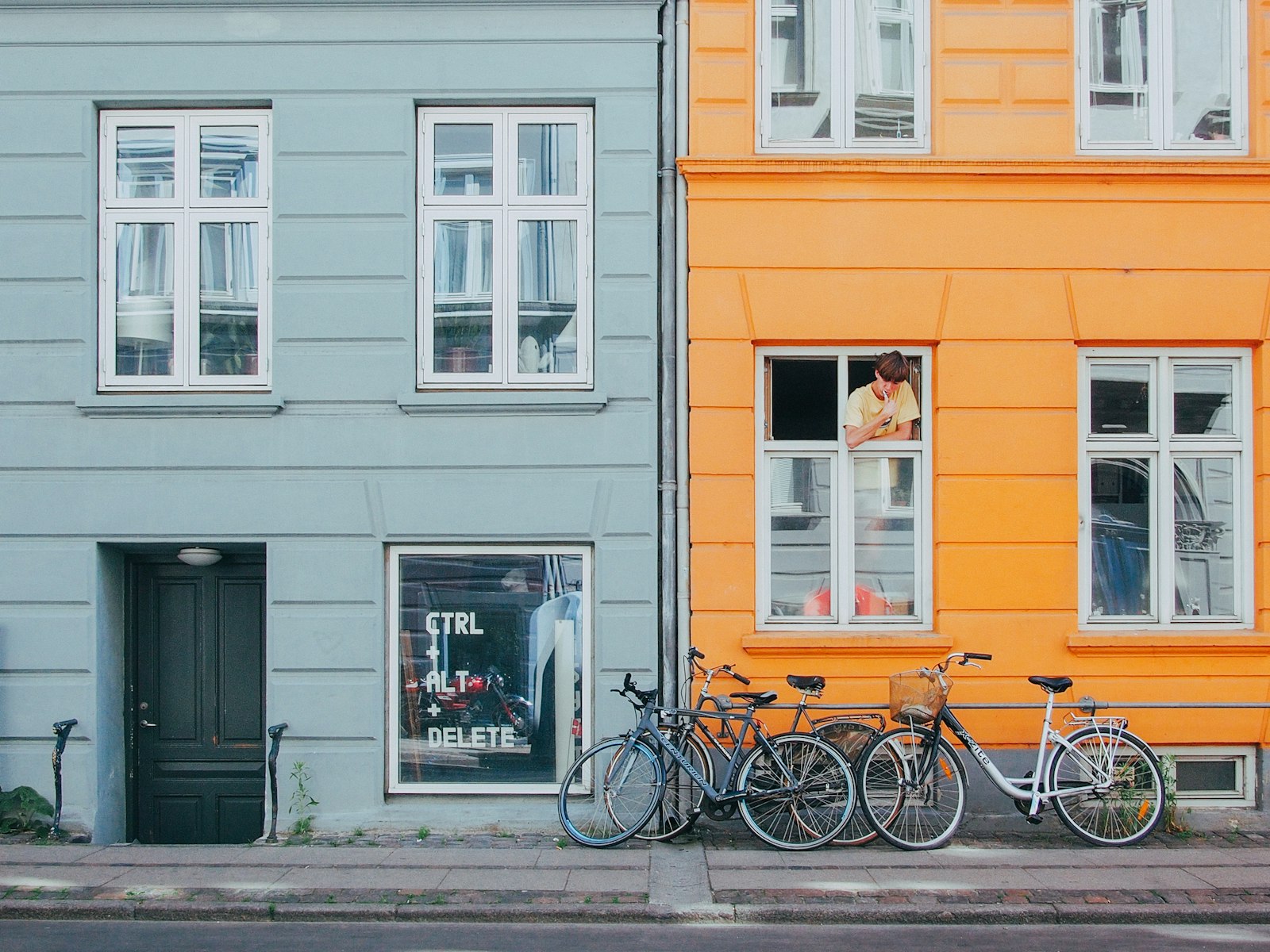 Bikes parked along a row of orange and grey-blue townhouses on a Copenhagen residential street. Photo by Carlo Villarica on Unsplash.