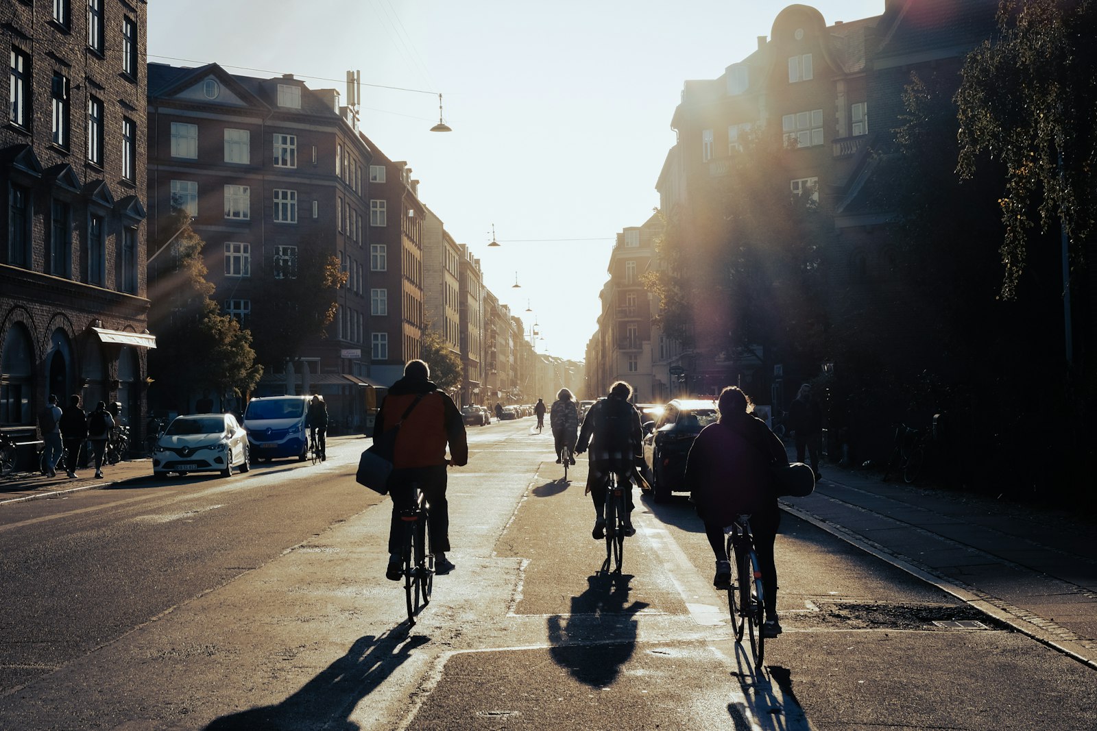 Cyclists riding in a bike lane down a sunlit Copenhagen street. Photo by Pedro Netto on Unsplash.