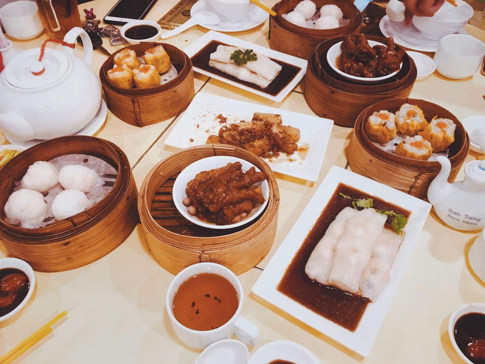 Una mesa compartida llena de dim sum vista desde arriba — vaporeras de bambú, dumplings y una tetera. Foto de Van Thanh en Unsplash.