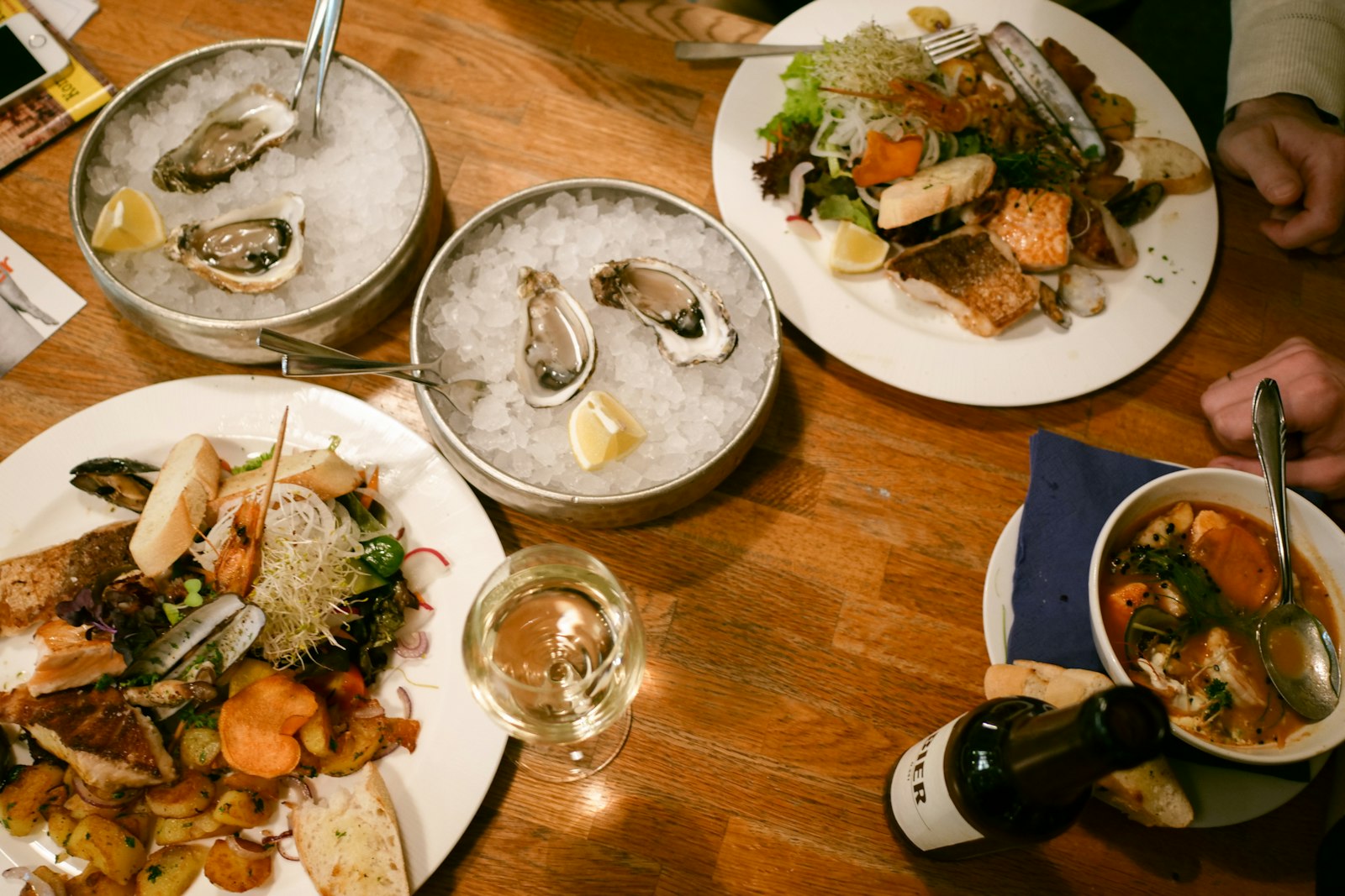 A shared table of oysters, seafood, and white wine at a harbourside restaurant. Photo by Kristina Tochilko on Unsplash.