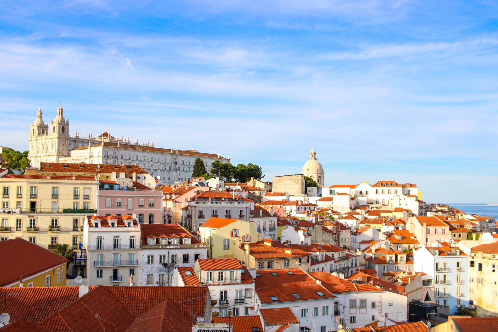 The rooftops and church domes of Alfama above the river in Lisbon. Photo by Guilherme Marques on Pexels.