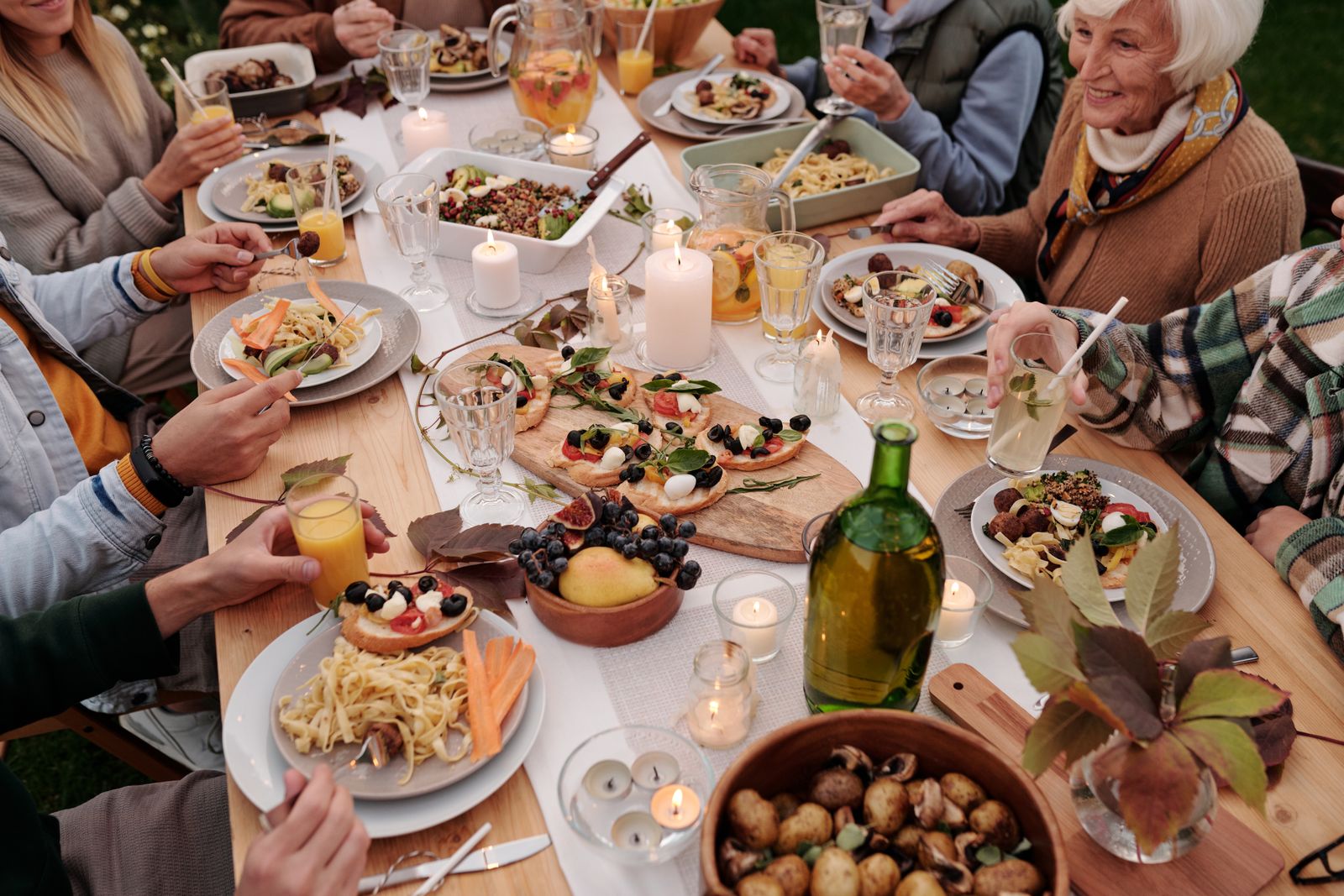 Hands reaching across a table crowded with shared plates. Photo by Askar Abayev on Pexels.
