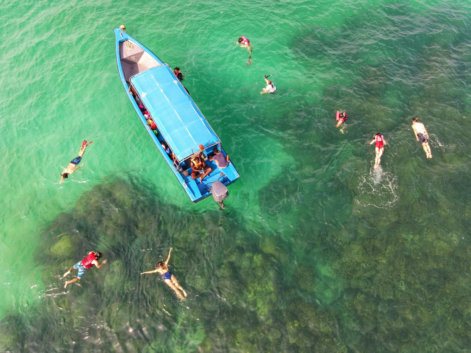 A small boat anchored in clear turquoise water with the group swimming off the back. Photo by Moe Mvp on Unsplash.