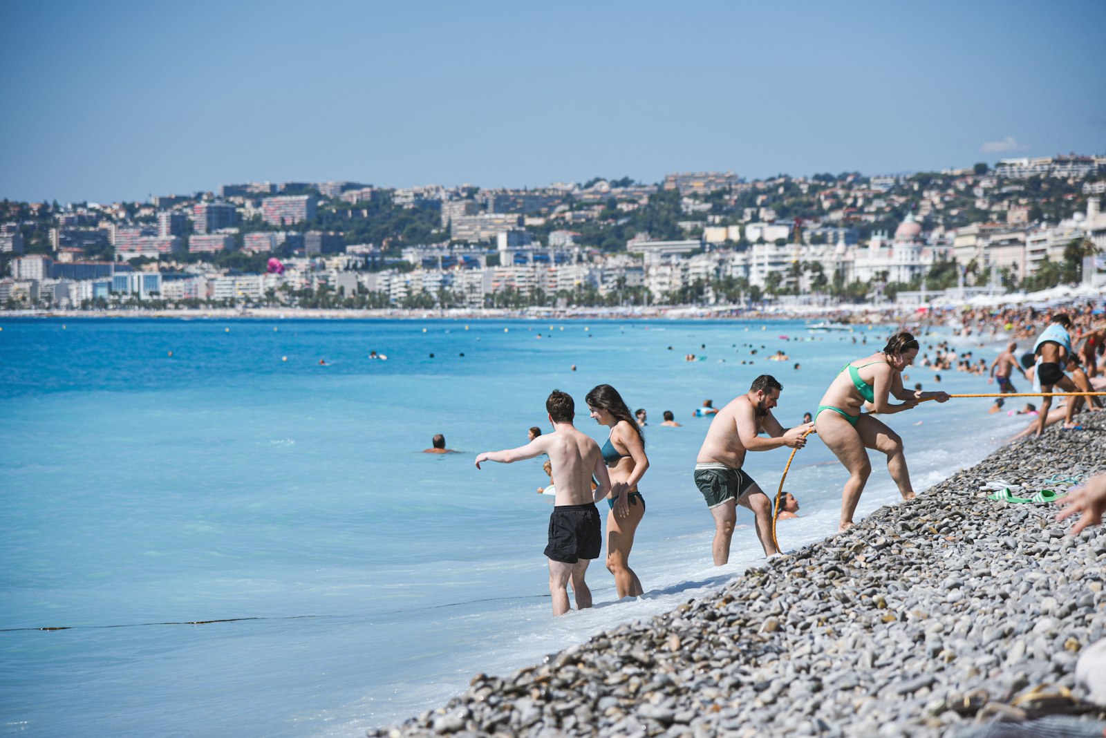 Groups swimming and sunbathing on the busy pebble beach and turquoise Baie des Anges at Nice. Photo by Luna Wang on Unsplash.
