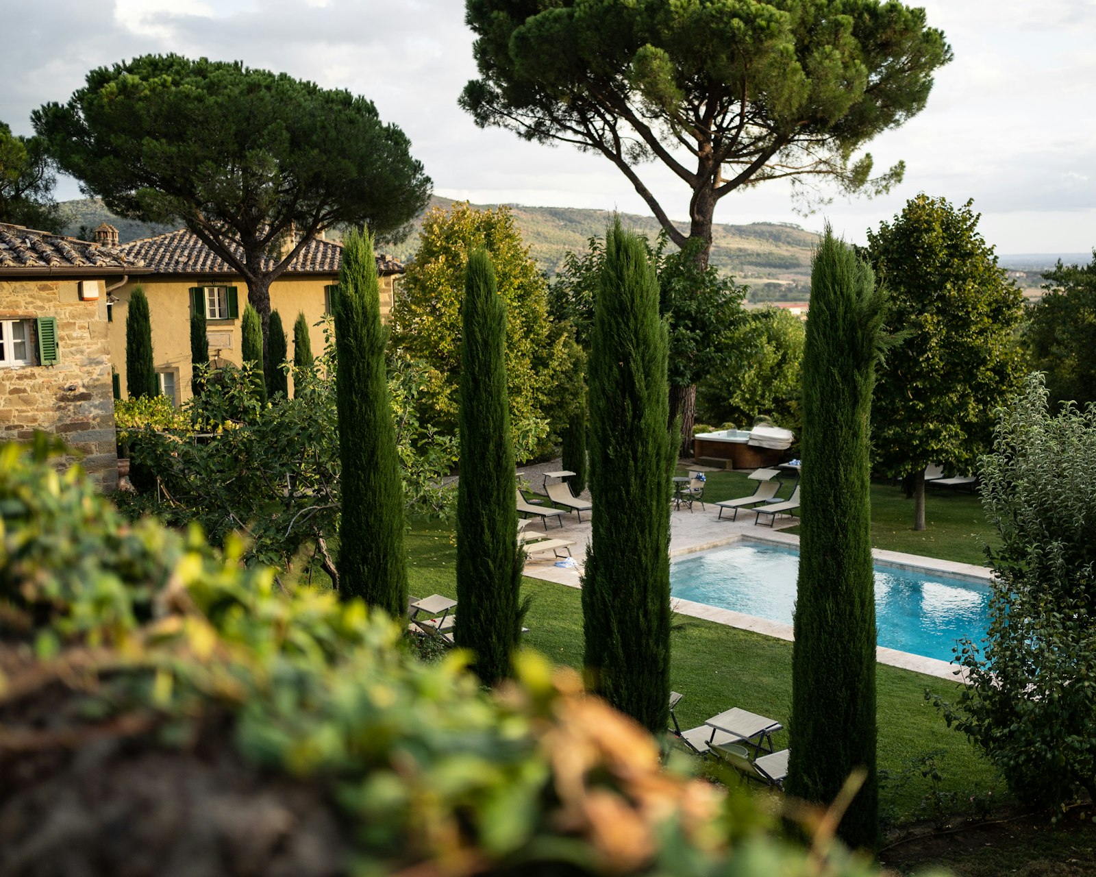 Una villa toscana de piedra con cipreses, pinos y una piscina en el jardín. Foto de Nick George en Unsplash.
