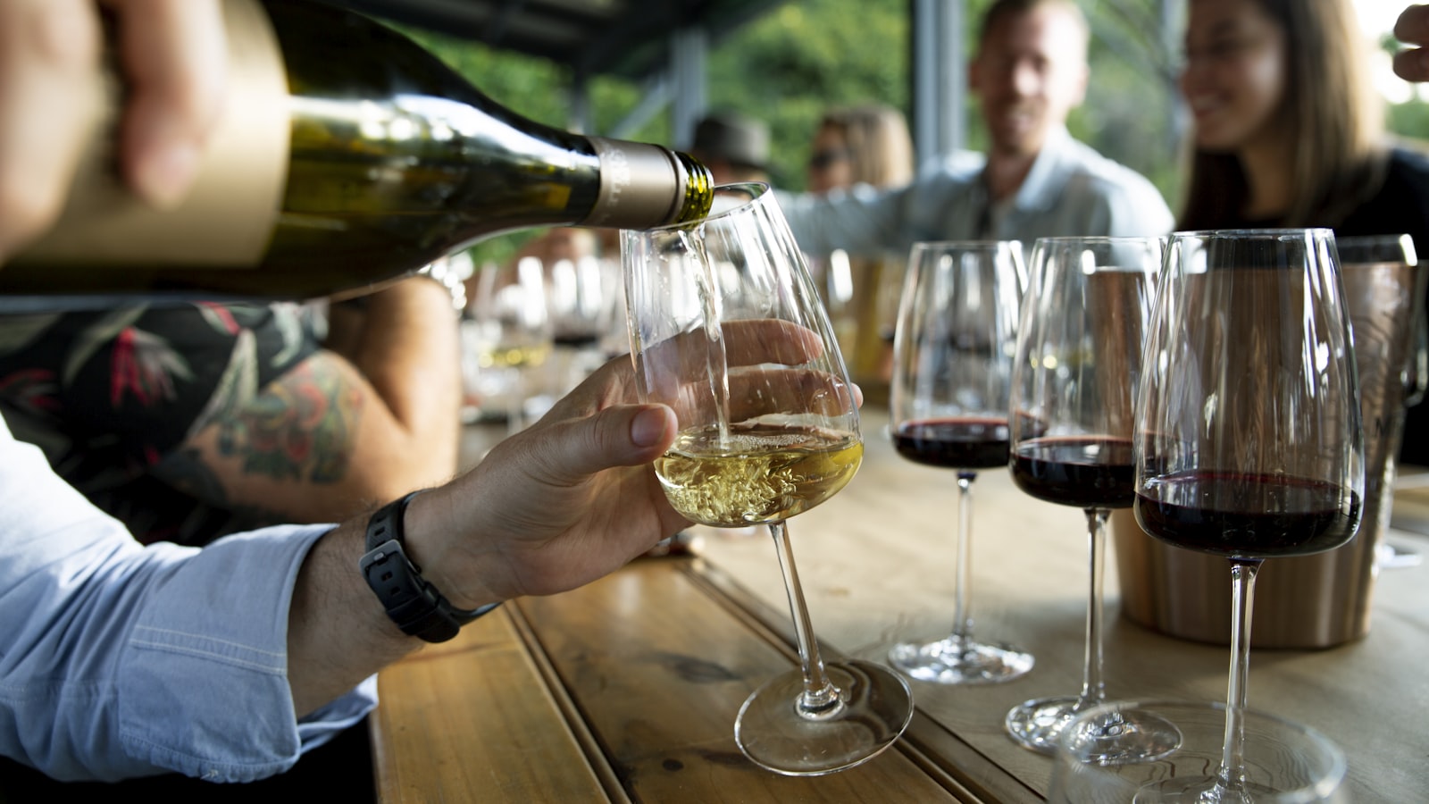 Vino blanco servido en una copa en una cata de grupo, con copas de tinto y blanco sobre la mesa. Foto de Caroline Attwood en Unsplash.
