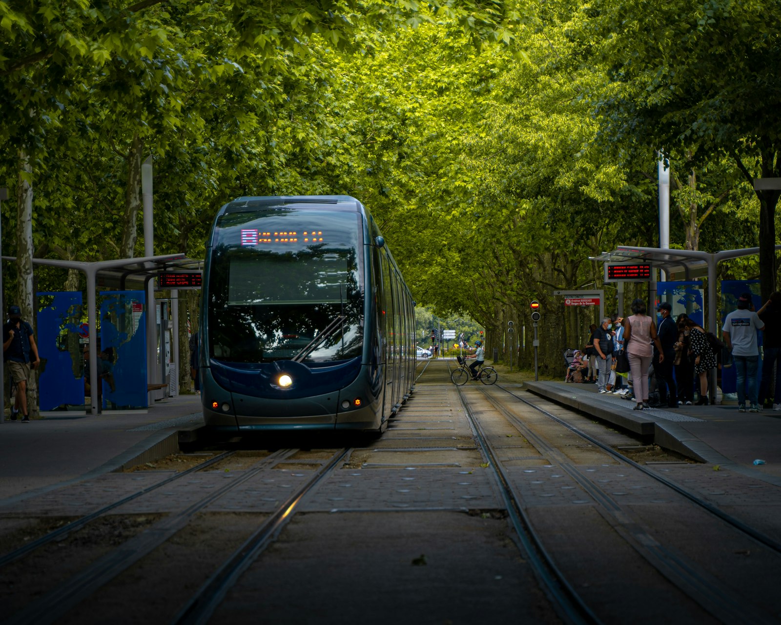 Un tranvía de Burdeos en una parada arbolada con pasajeros esperando en el andén. Foto de Anthony Persegol en Unsplash.