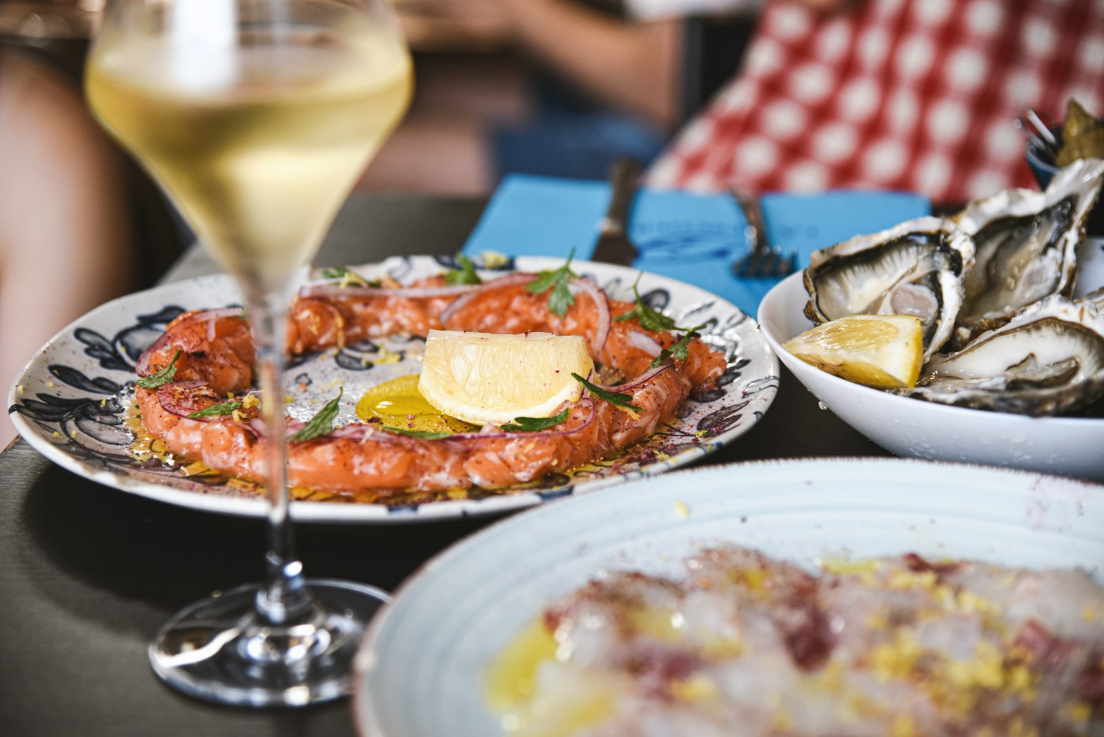 Una mesa con una copa de vino blanco frío, ostras frescas y pequeños platos de mariscos. Foto de Luna Wang en Unsplash.