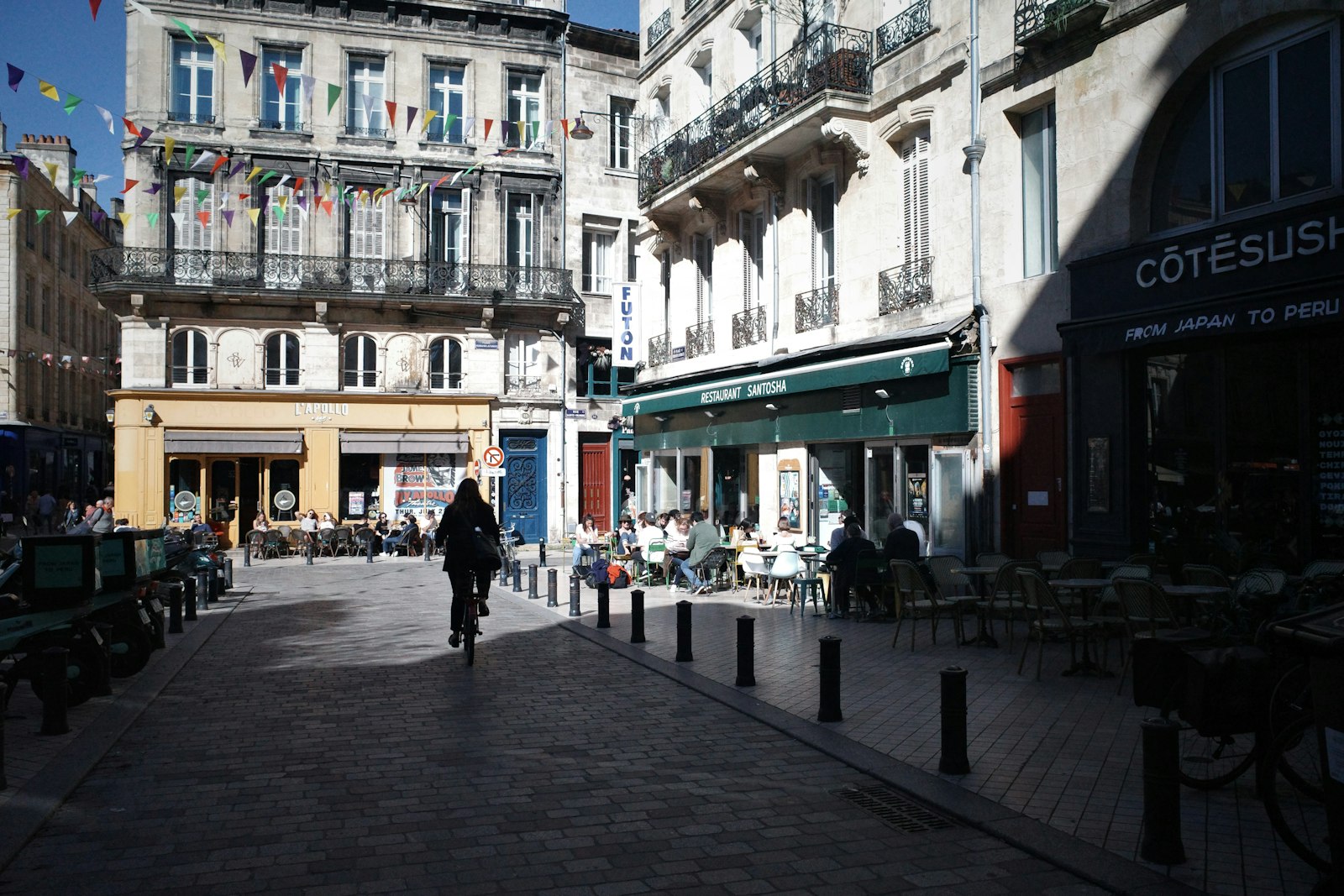 Una esquina animada del casco antiguo de Burdeos, con terrazas de café y un ciclista entre edificios de piedra color miel. Foto de Fantine Chance en Unsplash.