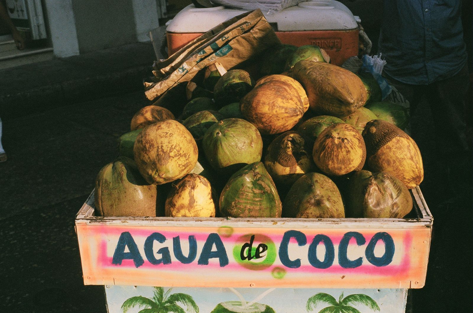 A street cart stacked with green coconuts under a hand-painted agua de coco sign in Cartagena. Photo by Maps Acosta on Pexels.