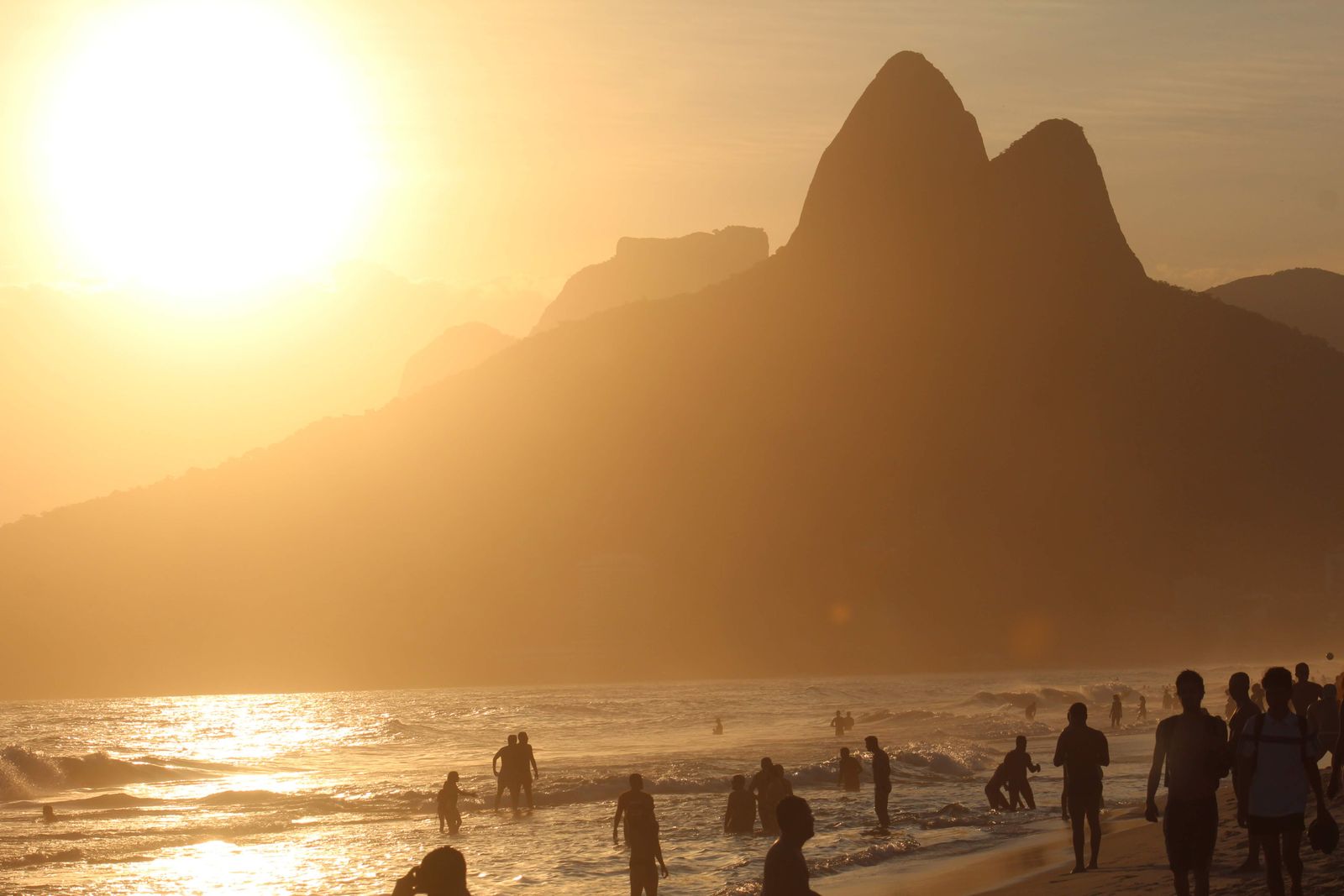 El sol bajando detrás de los morros Dois Irmãos con gente todavía en la playa. Foto de Eric Garcia en Pexels.