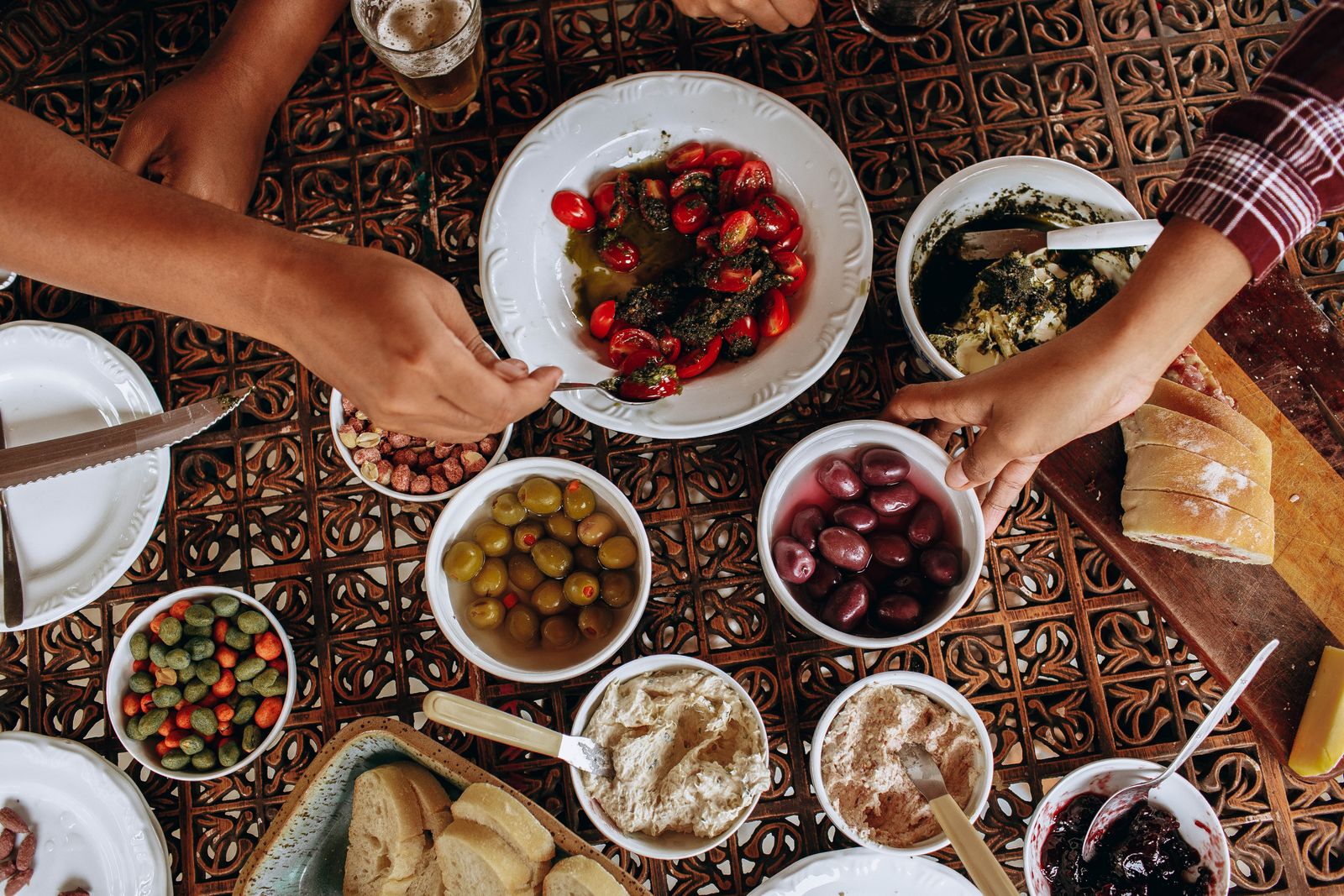 An overhead view of a long table of shared dishes with hands reaching across it. Photo by Helena Lopes on Pexels.