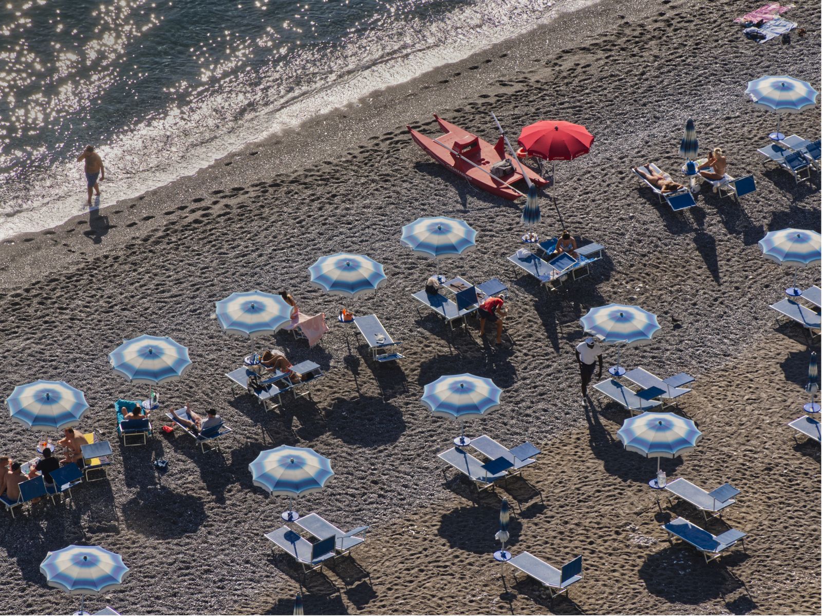 Rows of rented sun loungers and parasols on the sand, seen from above. Photo by Abdus Samad Mahkri on Pexels.