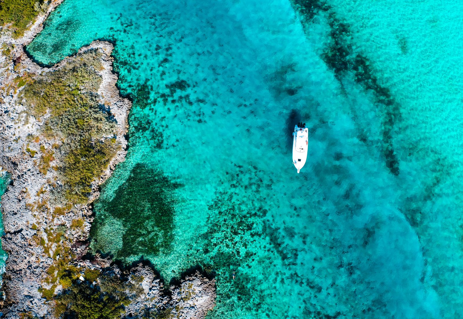 A small boat anchored over bright turquoise water off a rocky shore, seen from above. Photo by Cam Green on Pexels.
