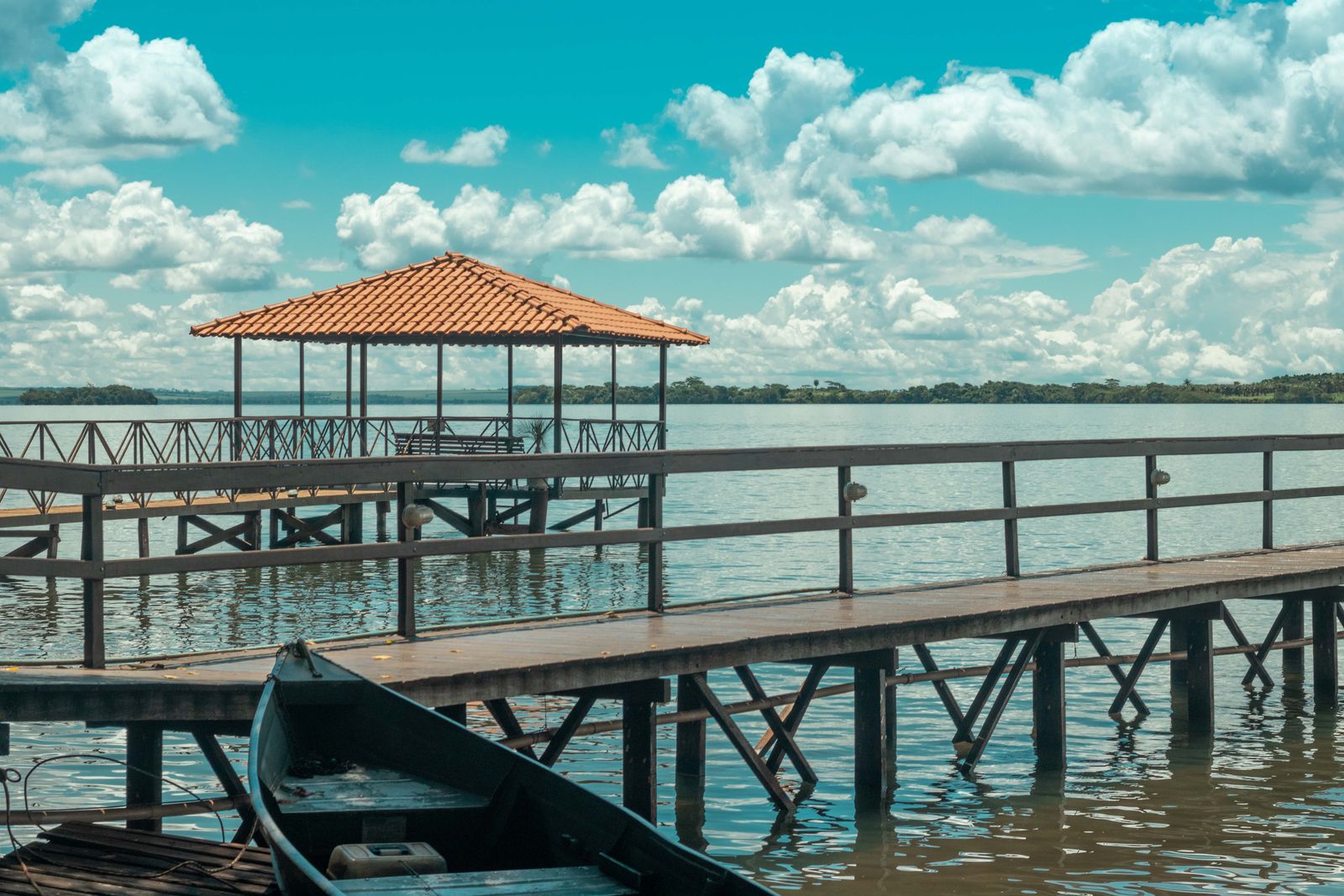 A wooden pier reaching out over flat, calm water, with a boat pulled up beside it. Photo by Kaio Cardim on Pexels.