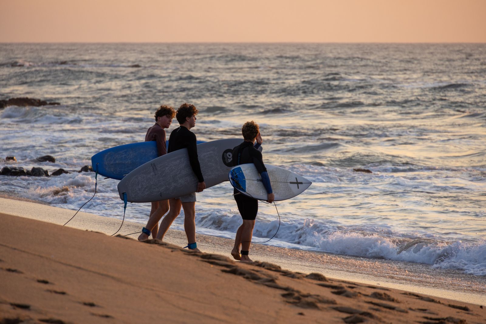 Three surfers walking down to the water carrying their boards. Photo by Magda Ehlers on Pexels.