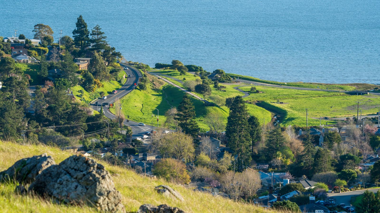 A road winding down a green coastal hillside towards the sea. Photo by ERod Photos on Pexels.