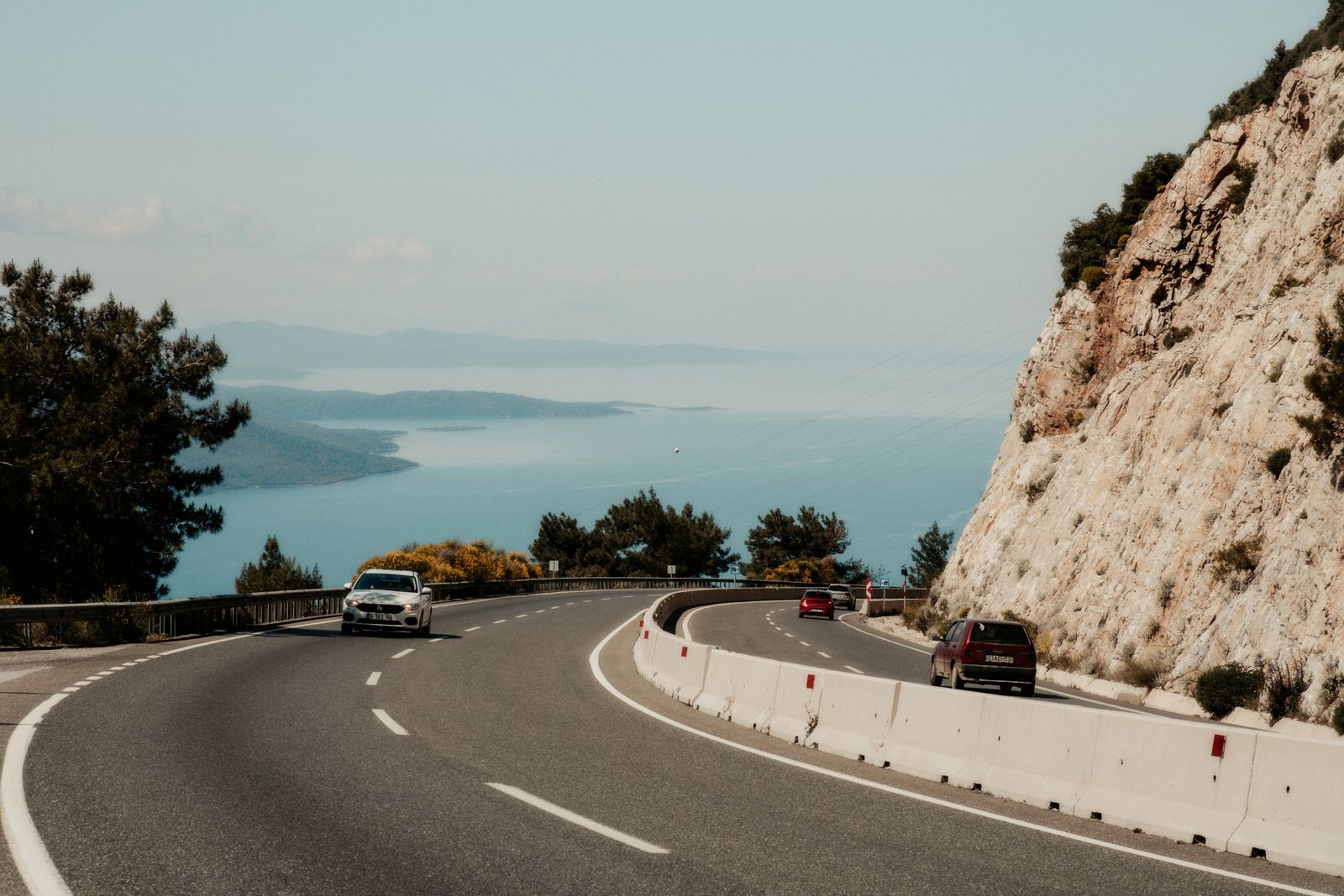 A winding coastal road with cars on it, above a wide blue bay. Photo by UMUT on Pexels.