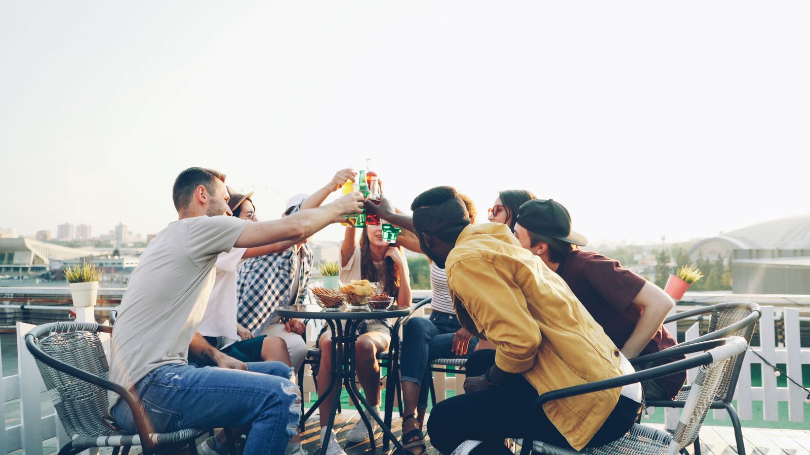 Amigos brindando con botellas alrededor de una mesa en una terraza. Foto de Vitaly Gariev en Pexels.