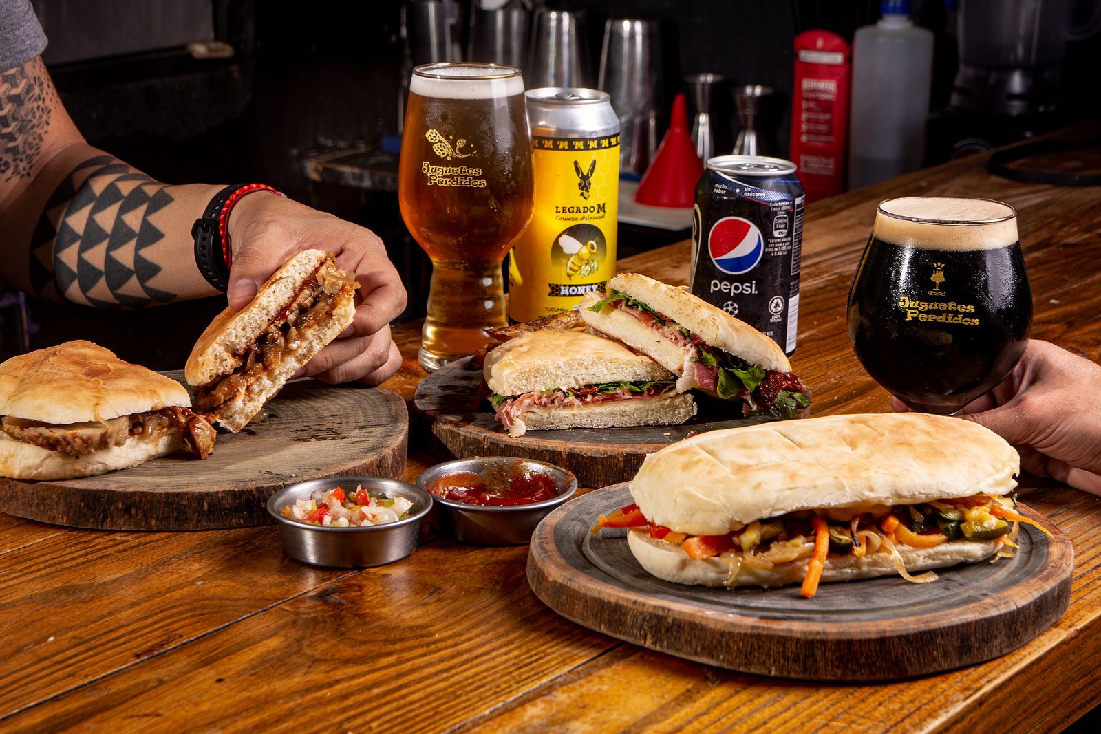 Dos sándwiches de lomo sobre tablas en la mesa de un bar, rodeados de bebidas. Foto de Gonzalo Acuña en Pexels.