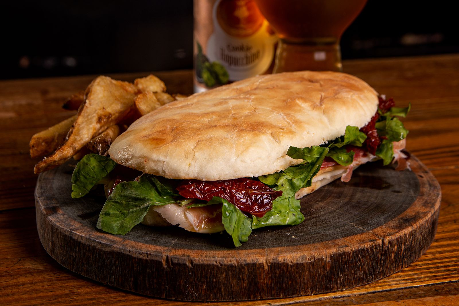 A large steak sandwich on a wooden board with a beer behind it. Photo by Gonzalo Acuña on Pexels.