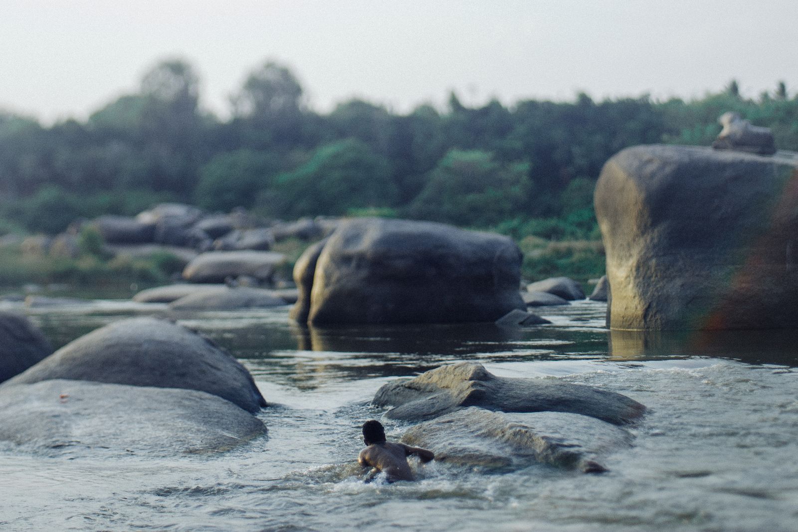 A river running between big granite boulders, one person swimming. Photo by Plato Terentev on Pexels.
