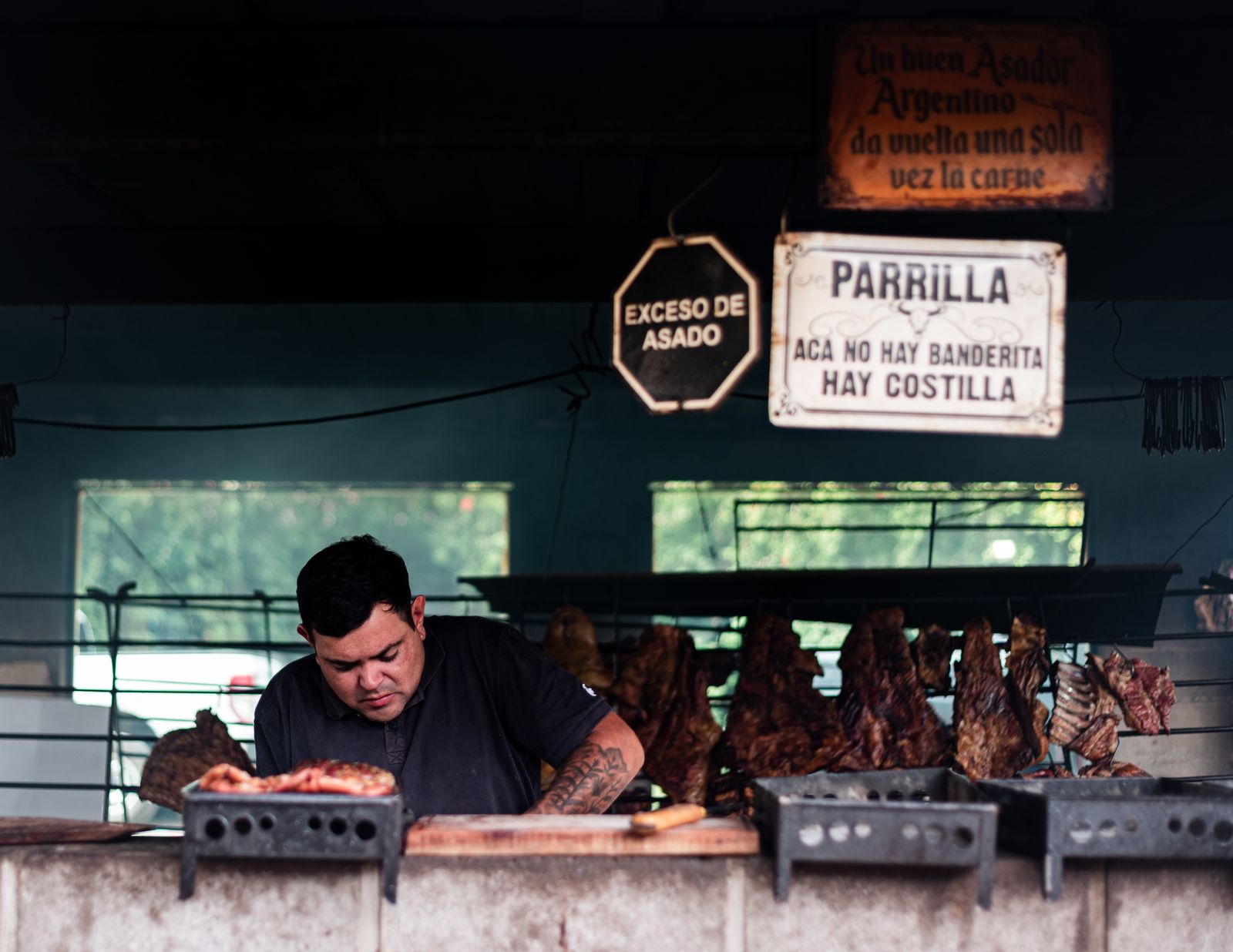 Un asador trabajando una parrilla a leña con costillares colgados. Foto de Alex Dos Santos en Pexels.