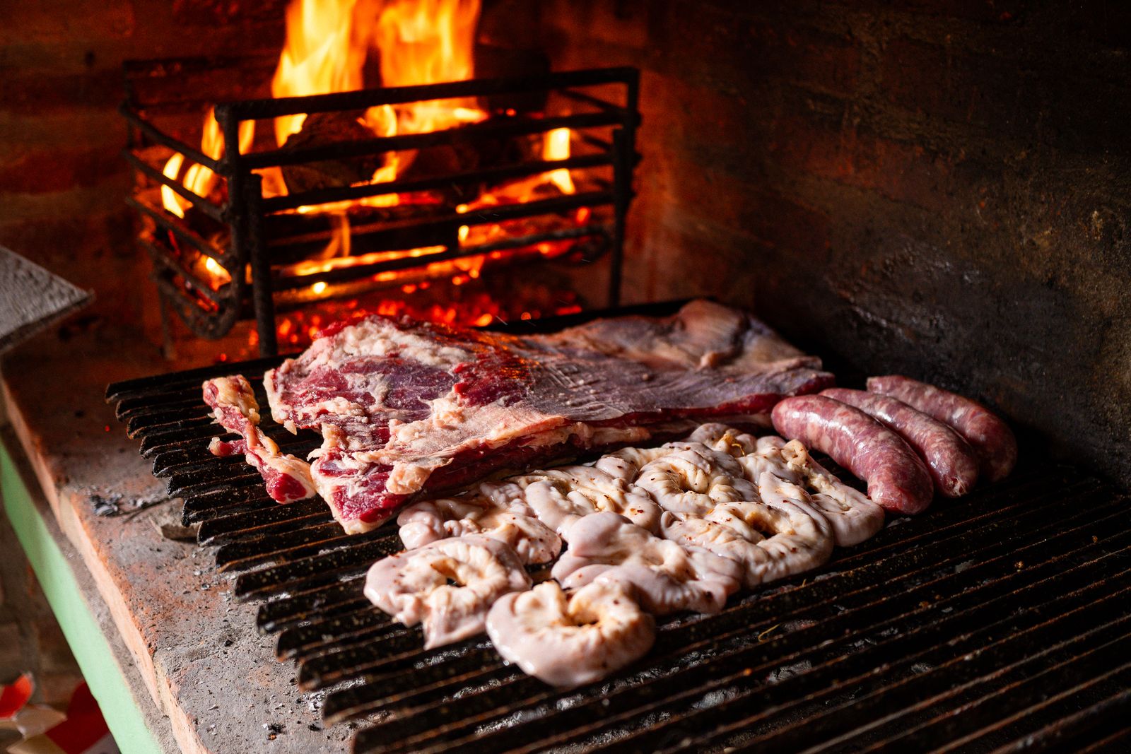 Ribs and chorizos cooking over a wood fire on a grill. Photo by Lucas Gramatica on Pexels.