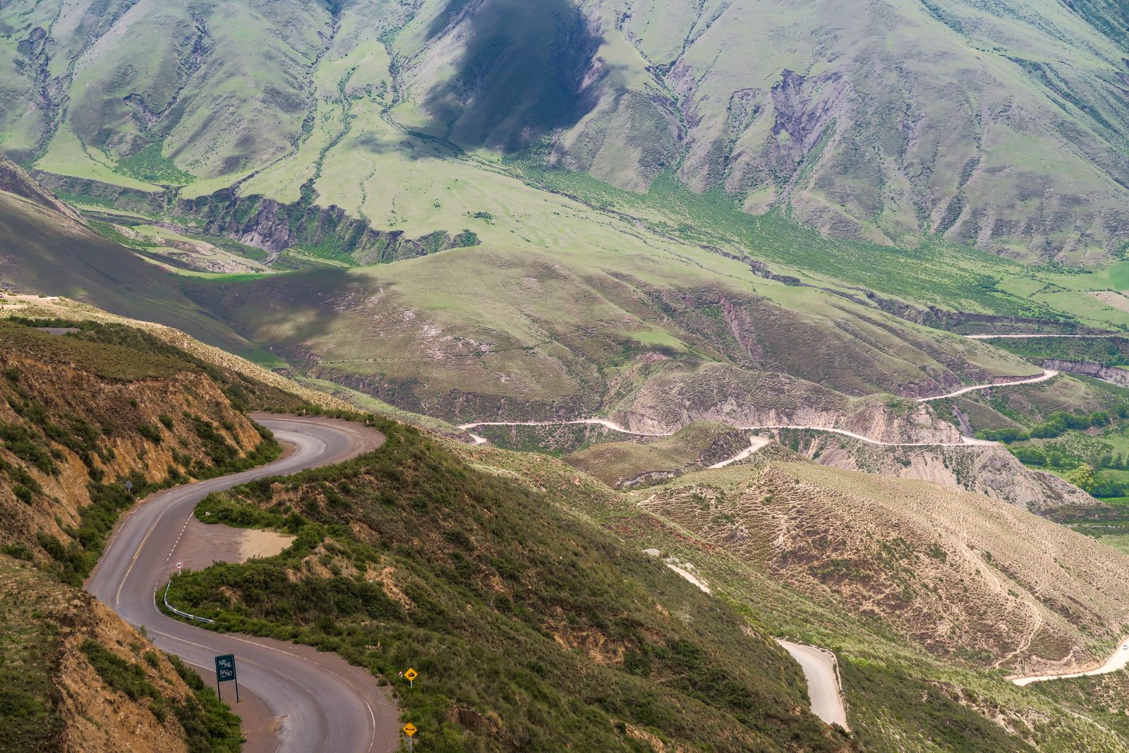 A road winding across open green-brown mountain slopes. Photo by Hector Perez on Pexels.