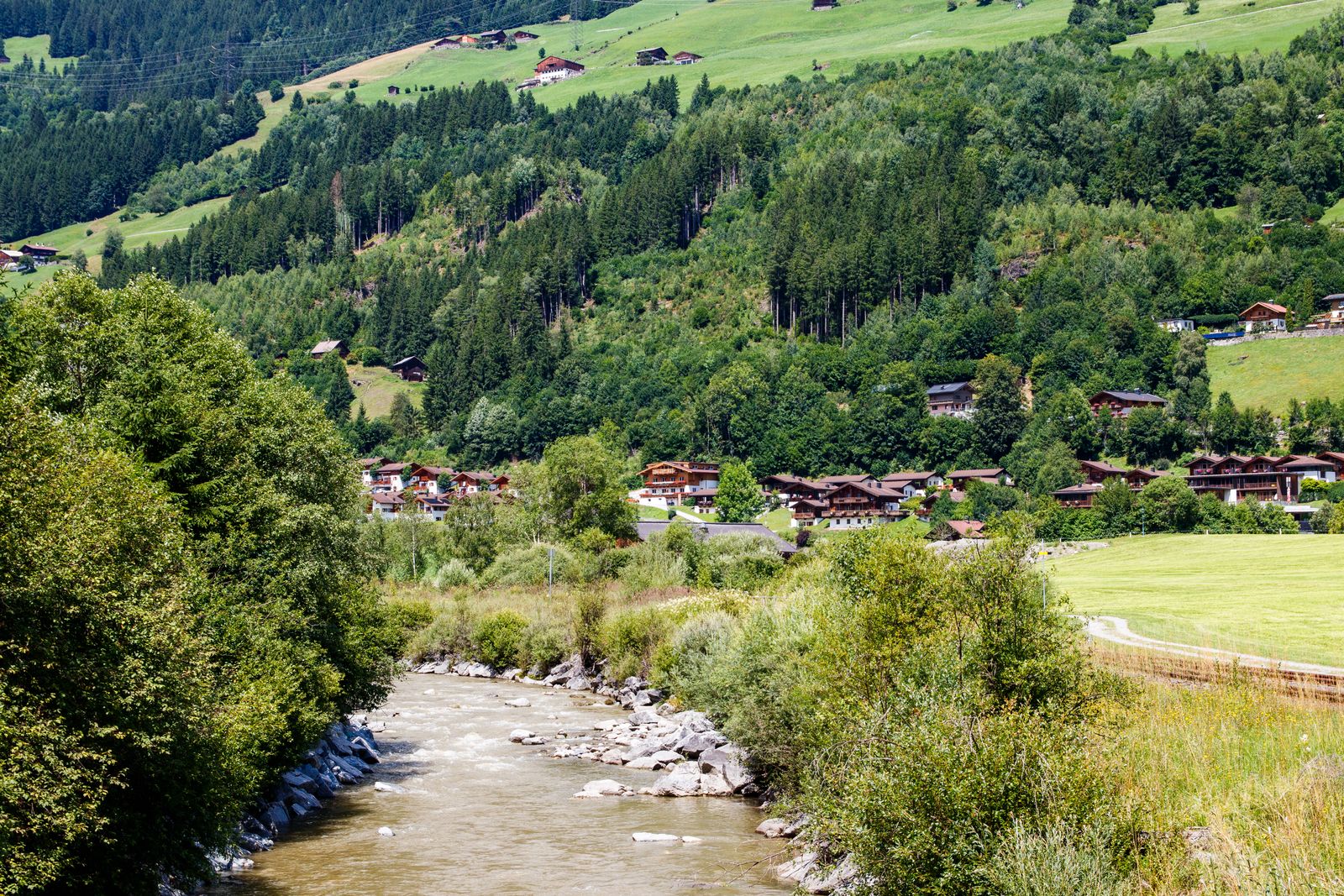 A green mountain valley with a river running past wooden houses. Photo by Freek Wolsink on Pexels.