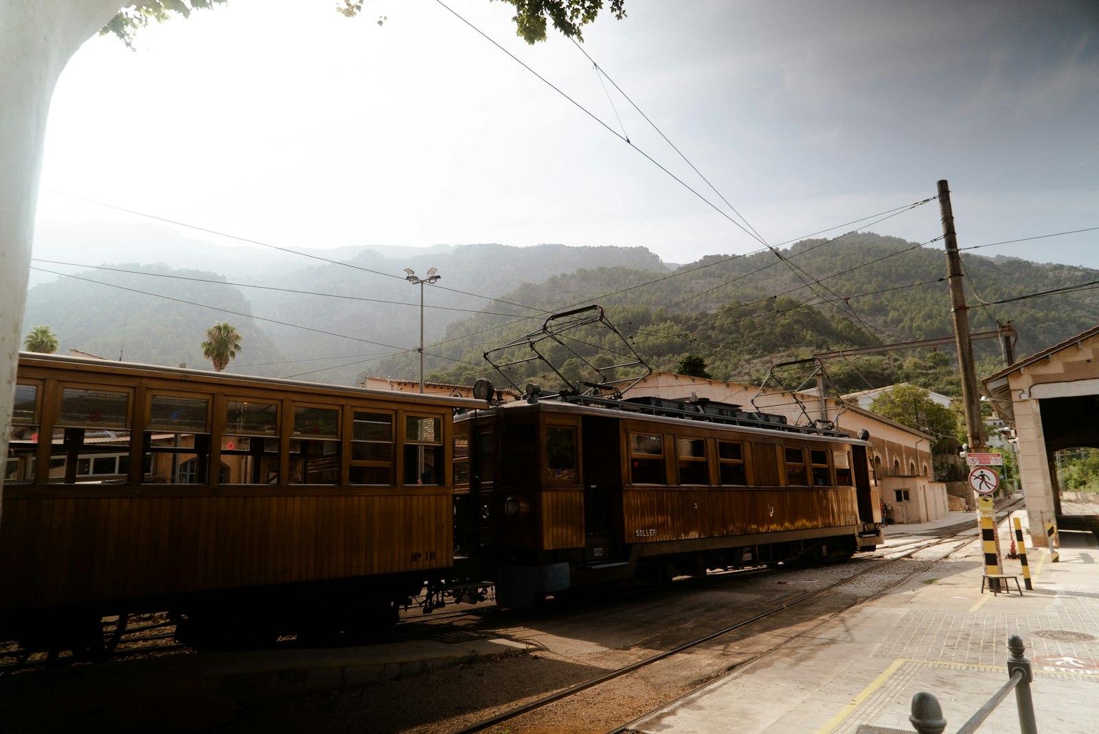 An older passenger train waiting at a small country station with hills behind. Photo by Victor Oonk on Unsplash.