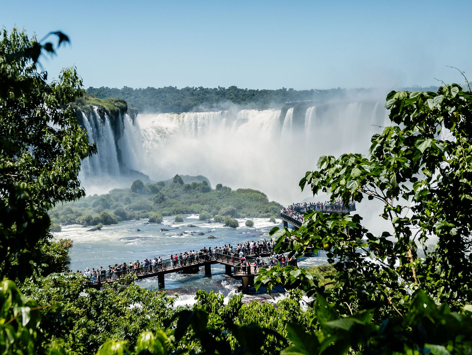 A crowded walkway below the falls, framed by green. Photo by Luriko Yamaguchi on Pexels.