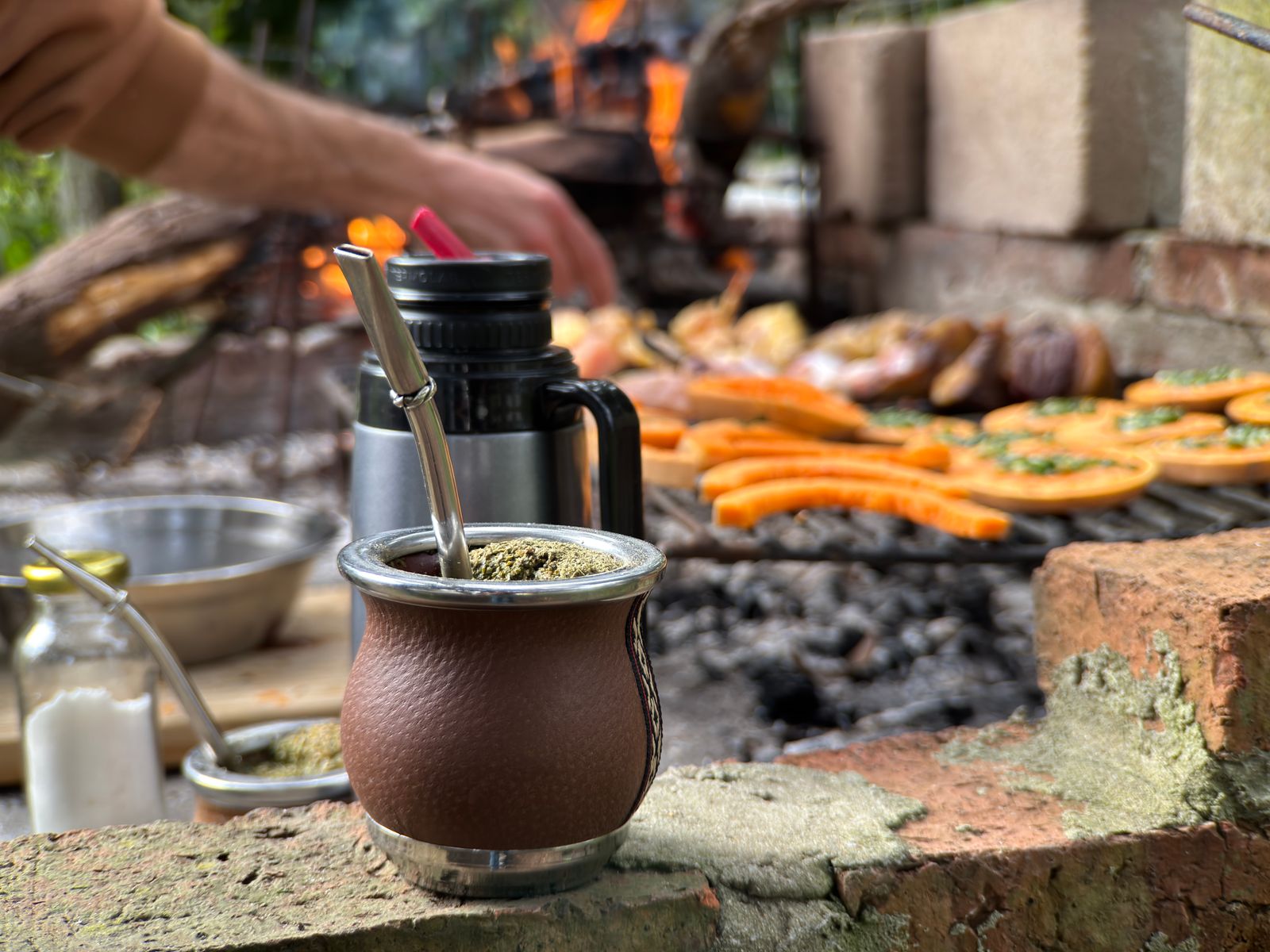 A mate gourd and thermos on stone beside a grill. Photo by Andrés Camacho on Pexels.