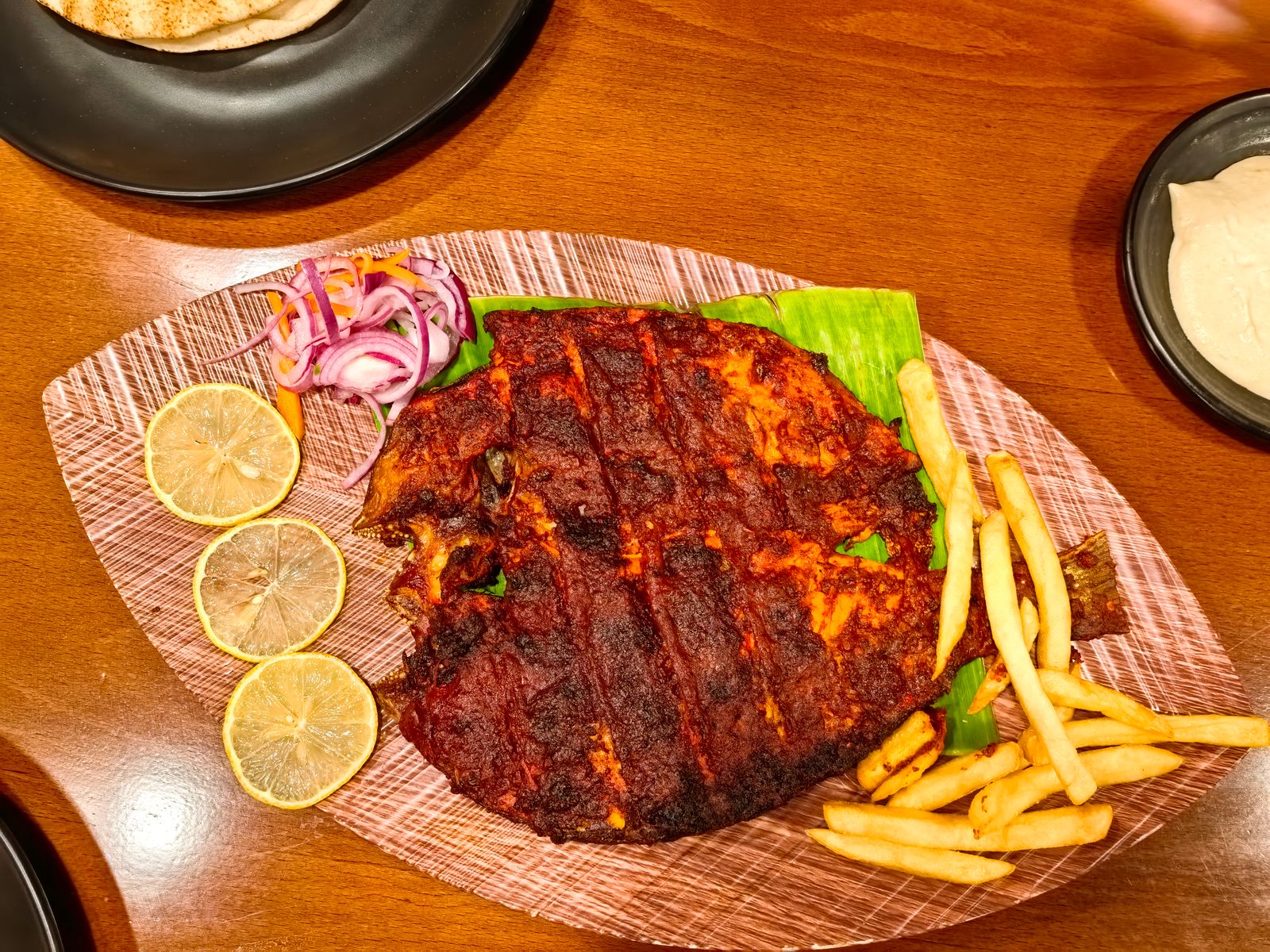 A whole grilled river fish on a board with lemon, onion and chips. Photo by Rafid k on Pexels.