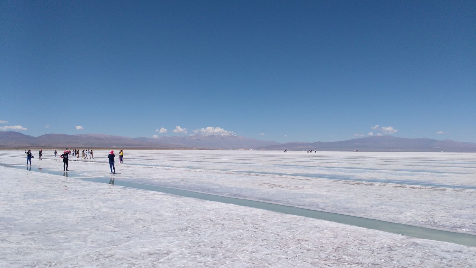 Un extenso salar blanco con gente caminando y montañas en el horizonte. Foto de Matias De Giorgio en Pexels.