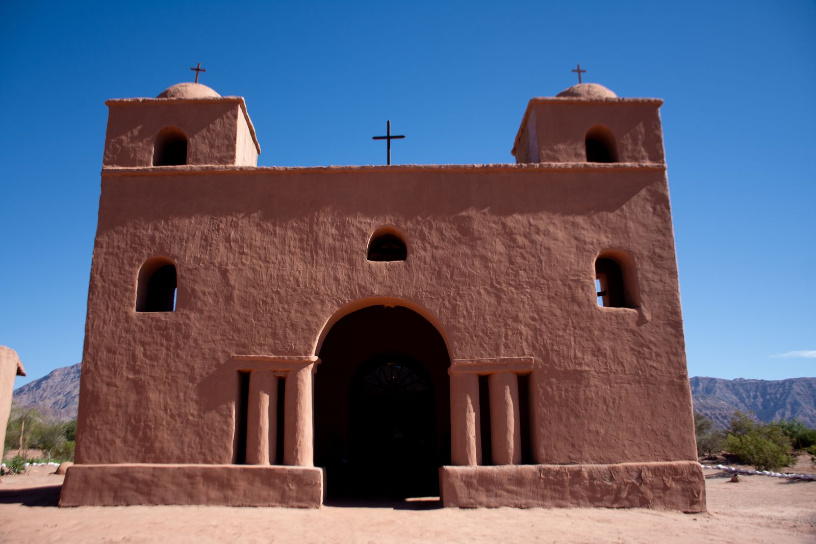 An adobe church with two bell towers against bare mountains. Photo by Patricia Bozan on Pexels.