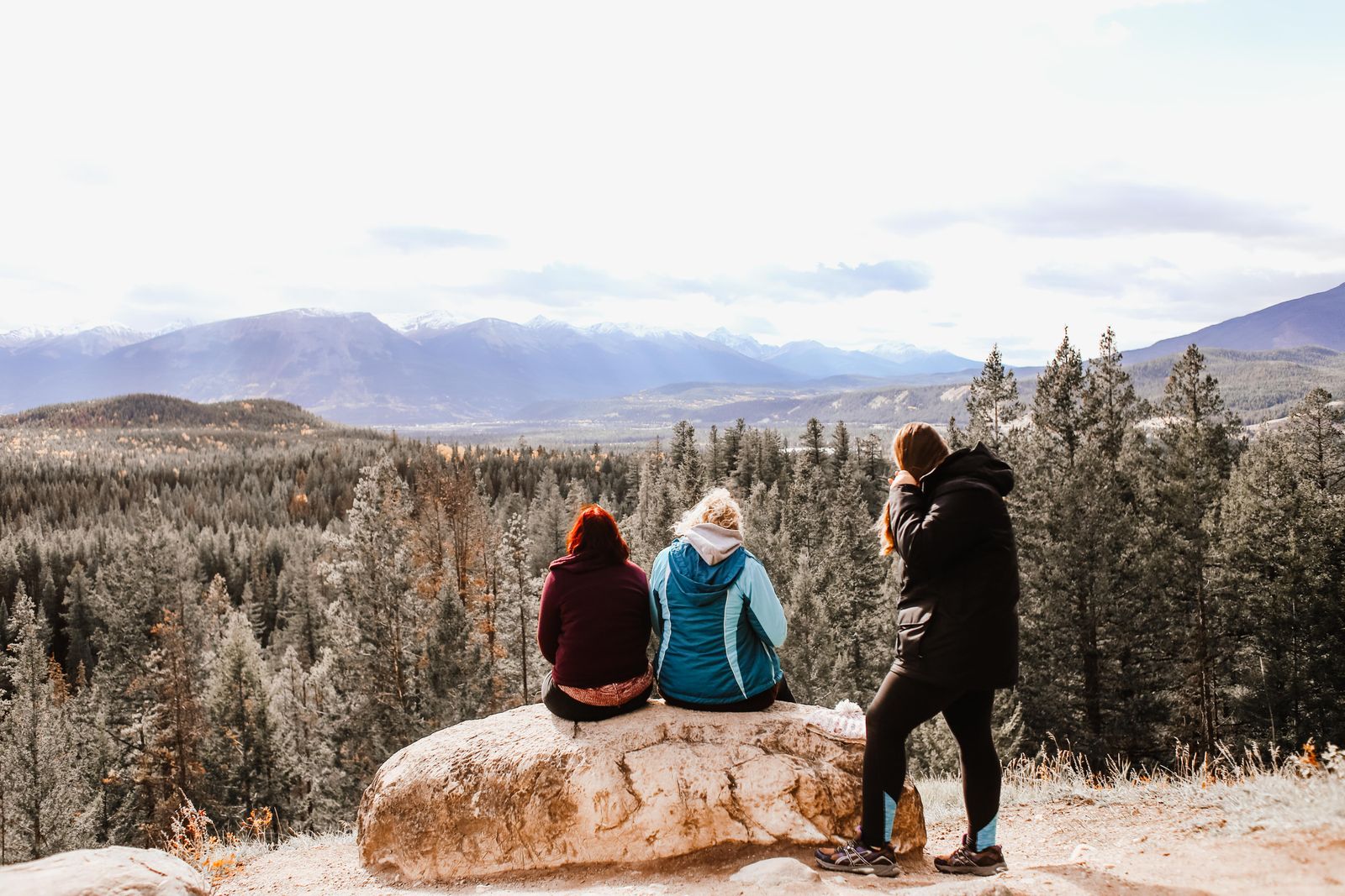 Tres personas sentadas en una roca mirando un amplio valle de montaña. Foto de Rachel Claire en Pexels.