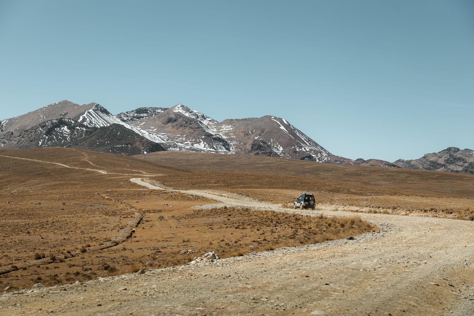 Un camino de ripio que cruza una planicie seca de altura hacia montañas lejanas. Foto de Gabriel Ramos en Pexels.