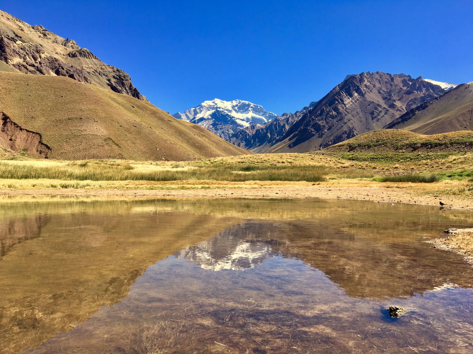 A snow-covered Andean peak reflected in a shallow lagoon on a dry valley floor. Photo by Claudio Mota on Pexels.