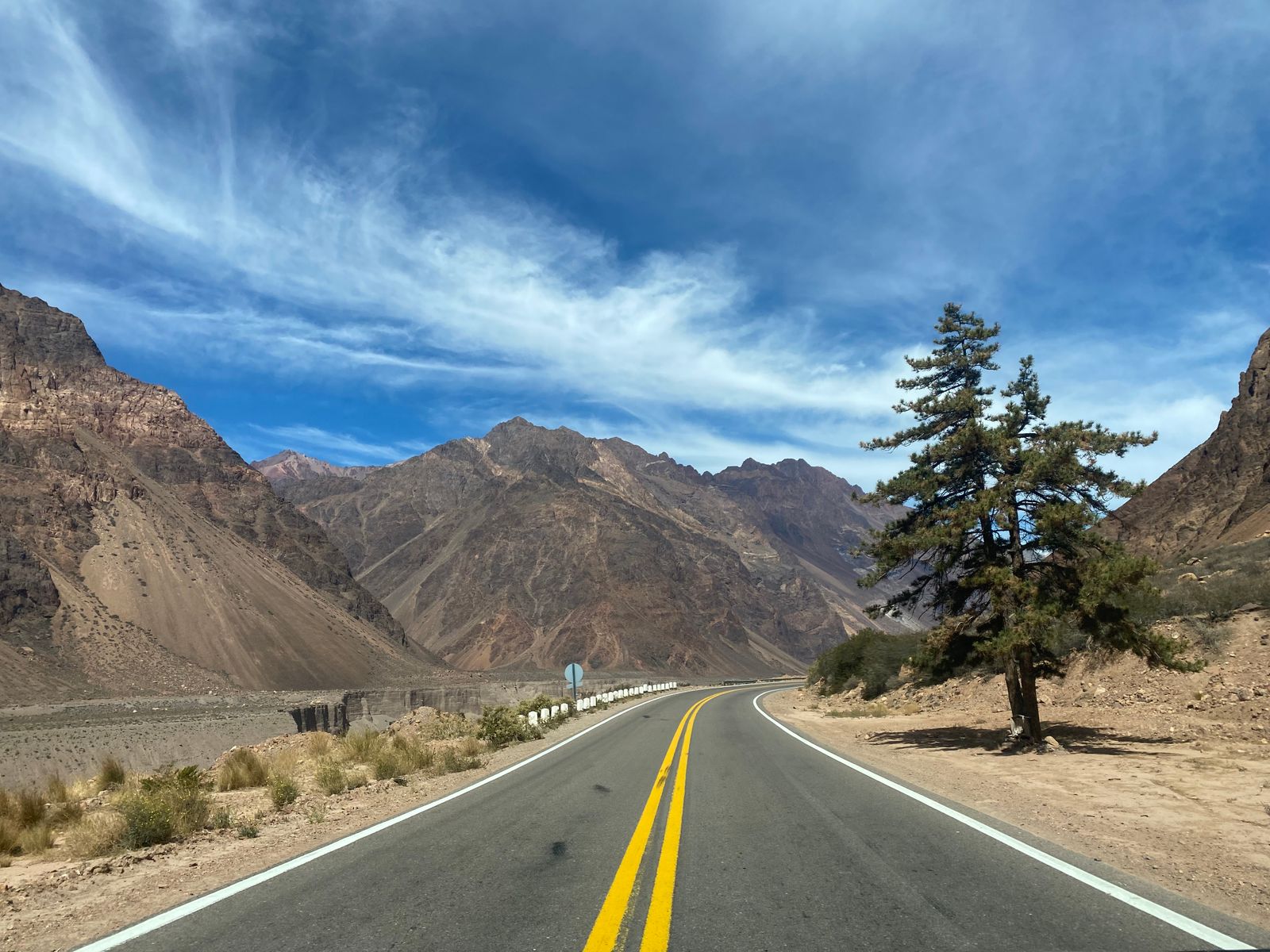 A straight road with a painted centre line heading into bare mountains. Photo by Danny Chang on Pexels.