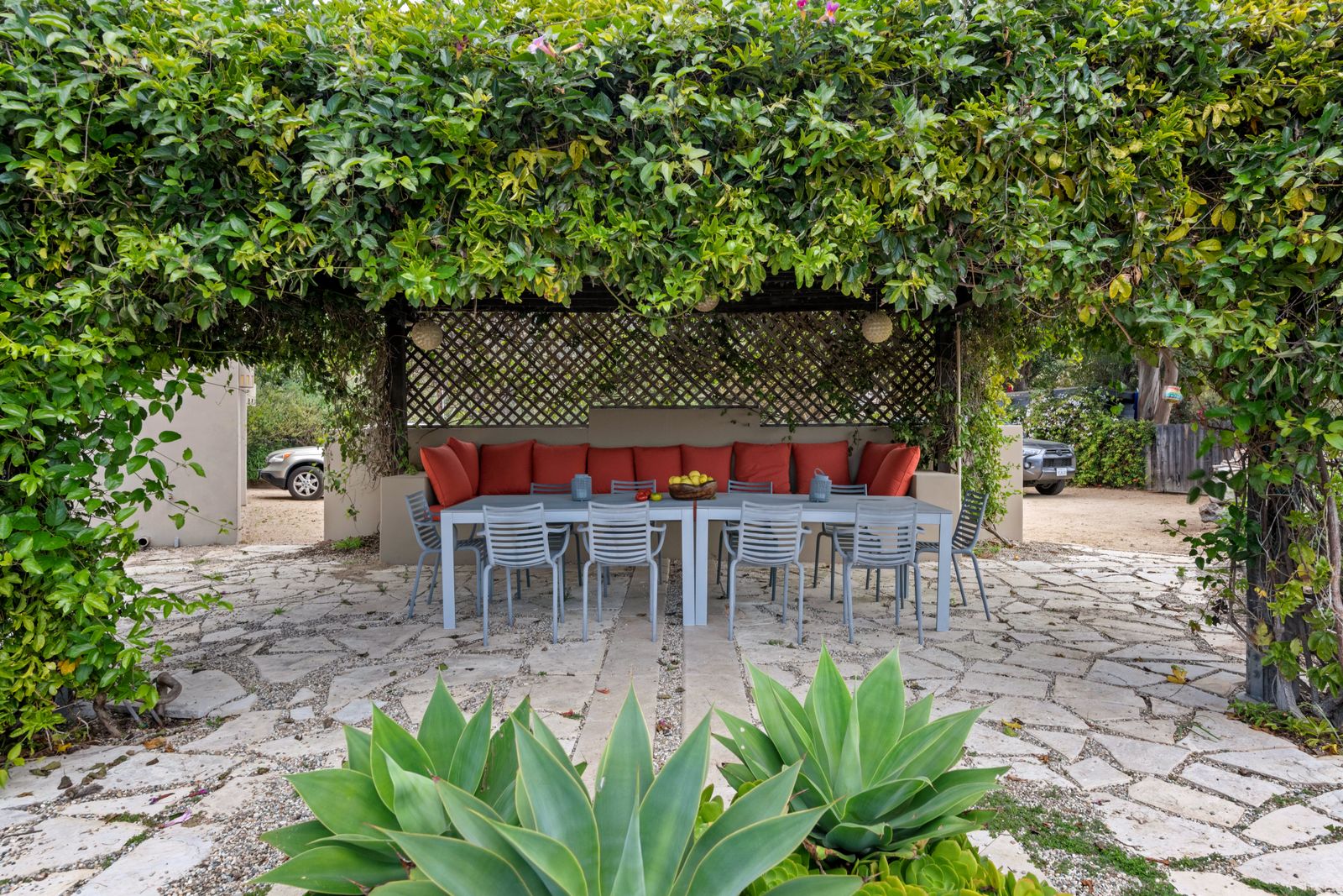 A long table set on a stone patio under a vine-covered pergola. Photo by hi room on Pexels.
