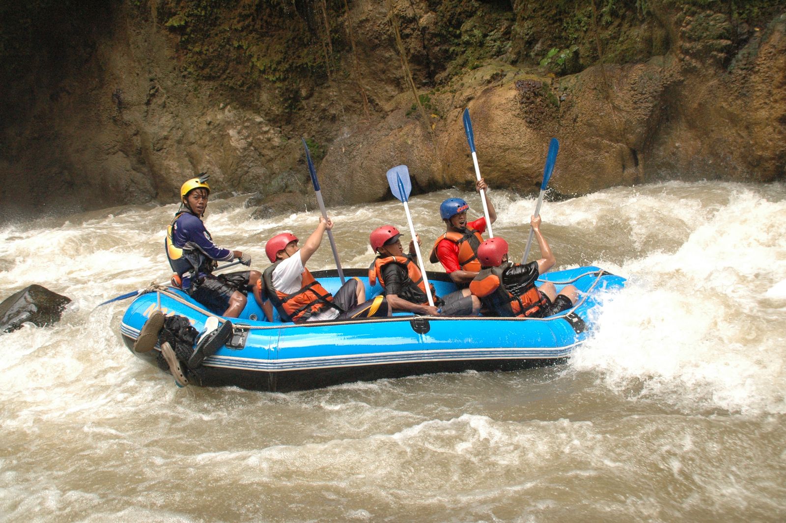 A raft of paddlers in helmets running through white water in a rocky gorge. Photo by Dawinara 23 on Pexels.
