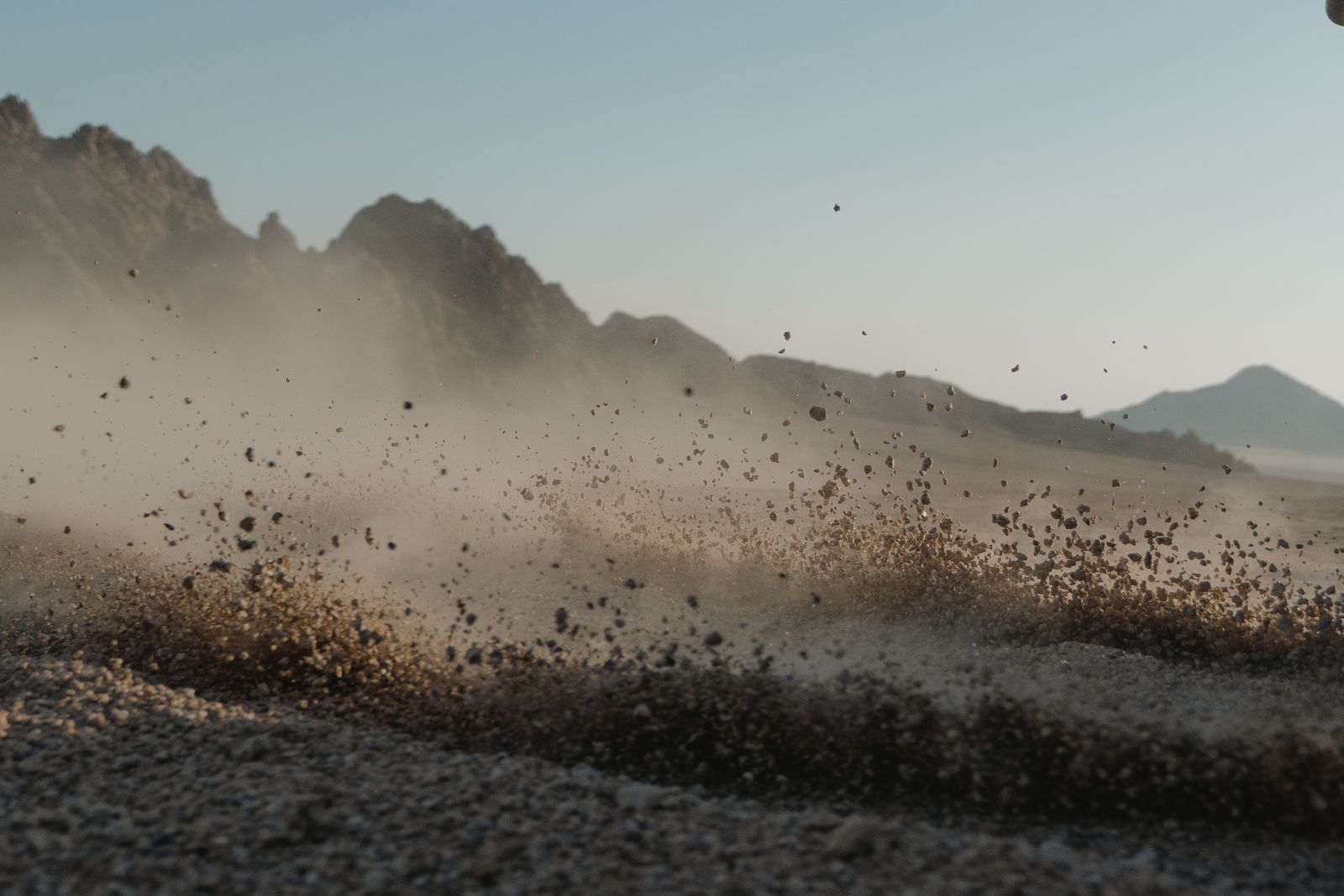 Dust and debris blowing across a dry slope below mountains. Photo by Tima Miroshnichenko on Pexels.