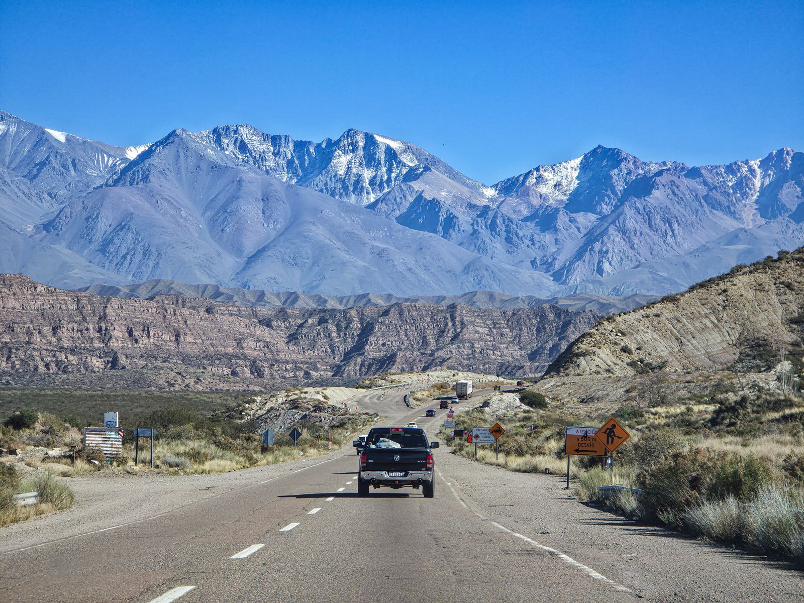A road running straight towards a wall of snow-covered Andean peaks. Photo by Lucas Porras on Pexels.